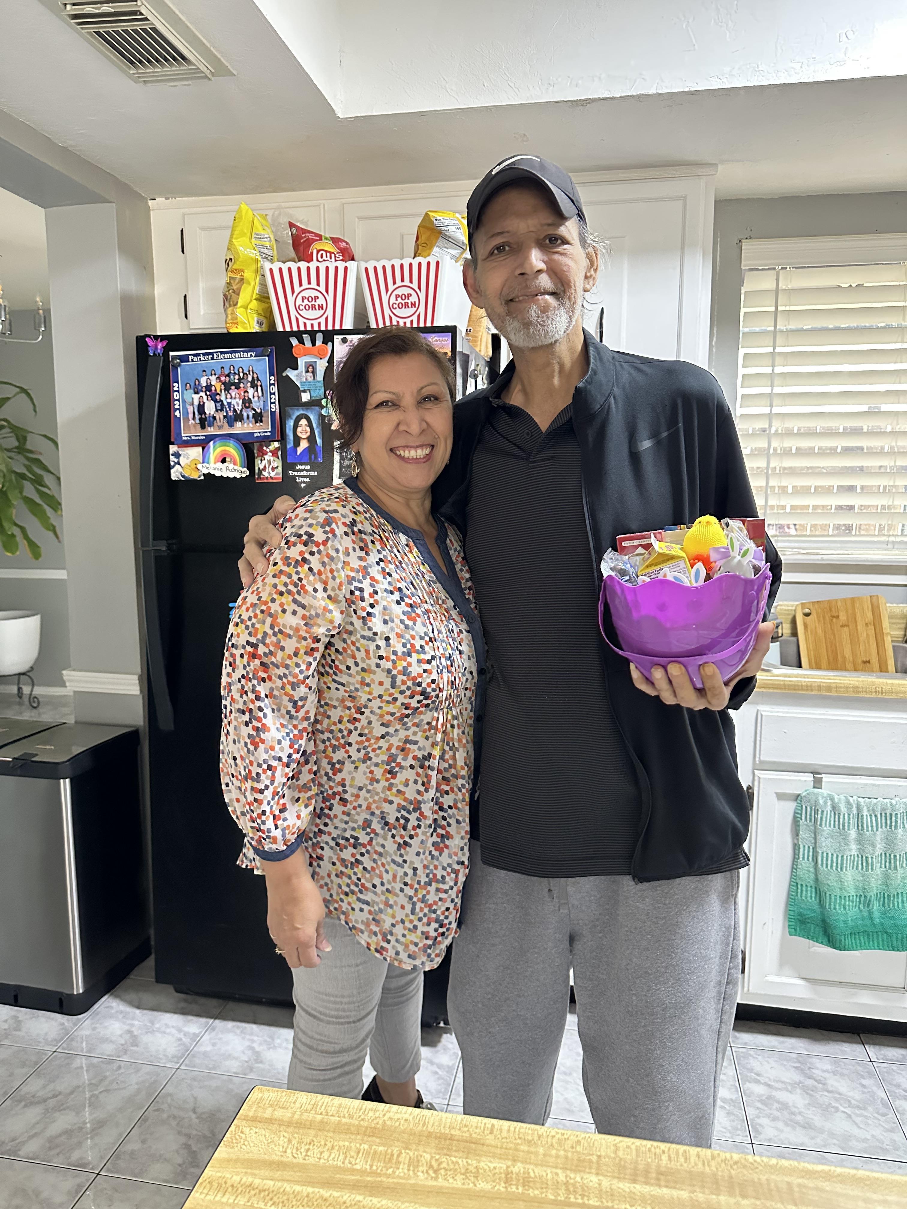 A man and woman standing in a kitchen holding a basket of food