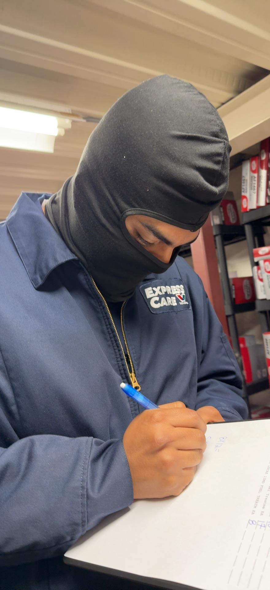 A man wearing a black mask writing on a clipboard