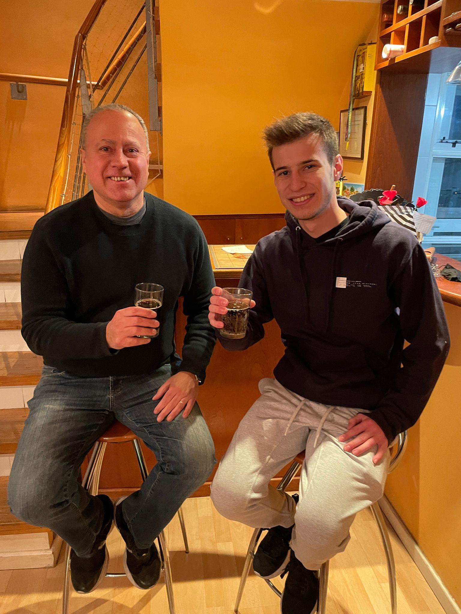 Two men sitting on stools holding drinks