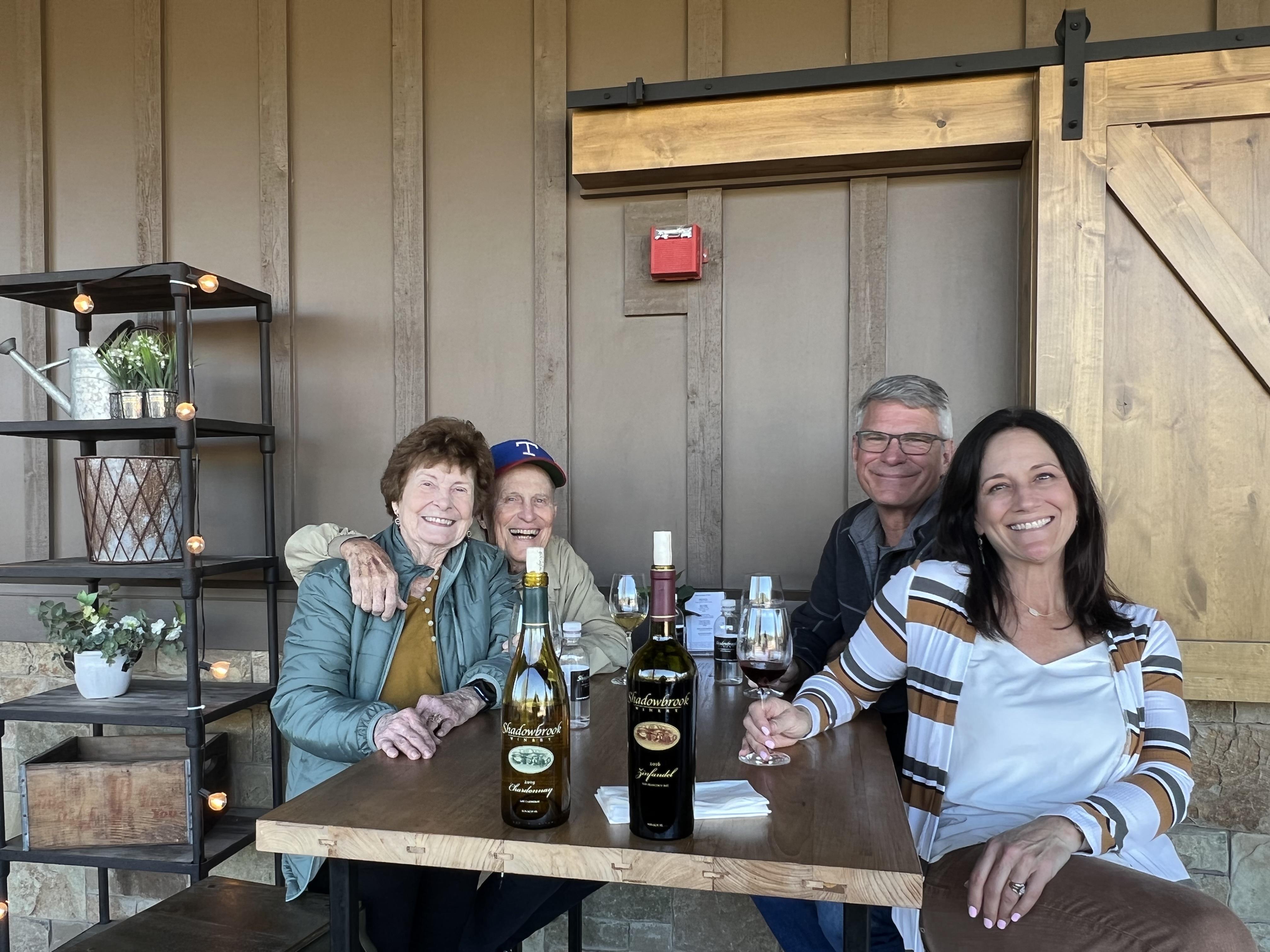 A group of people sitting at a table with bottles of wine