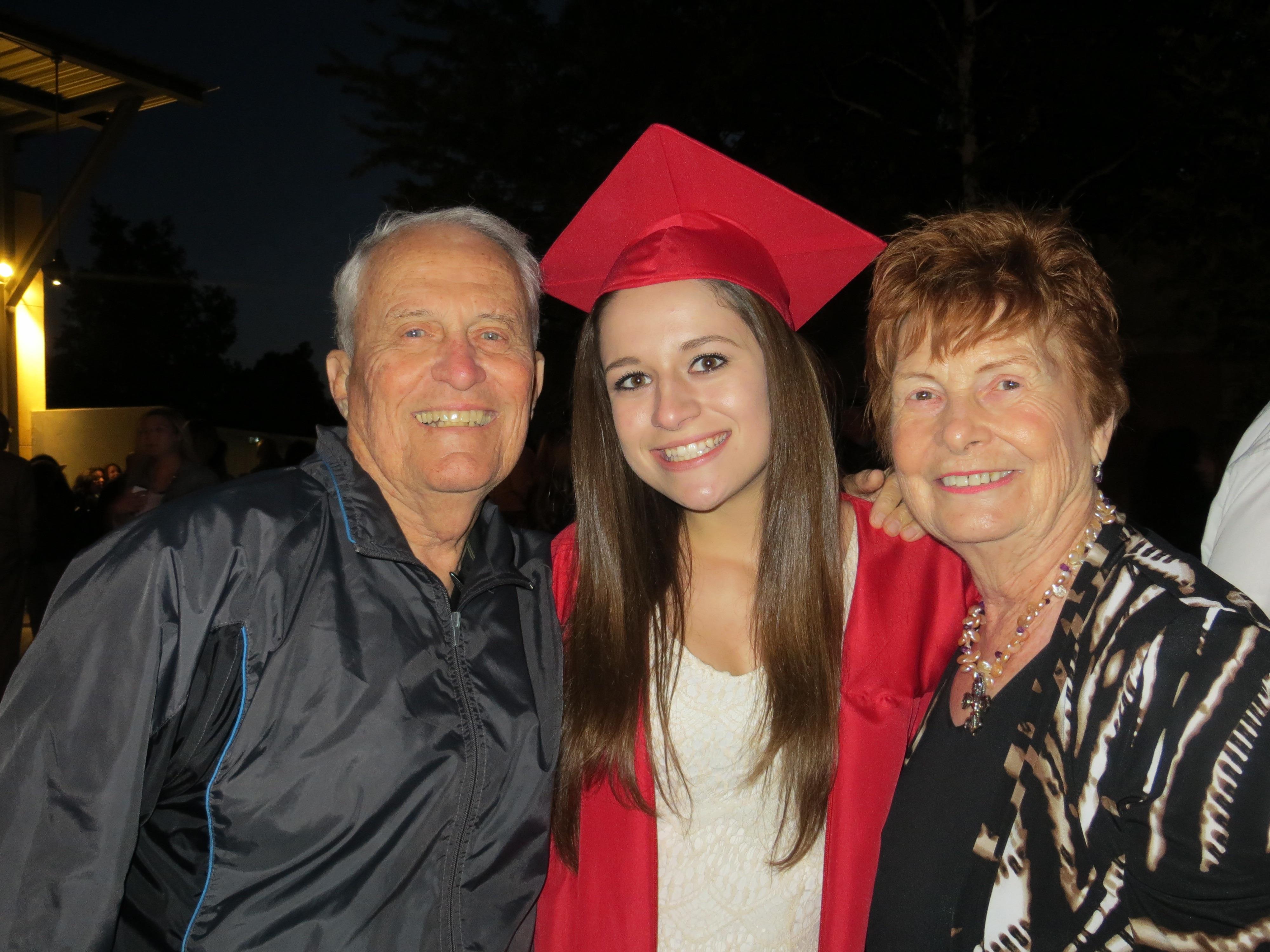 A woman in a graduation cap and gown with an elderly couple