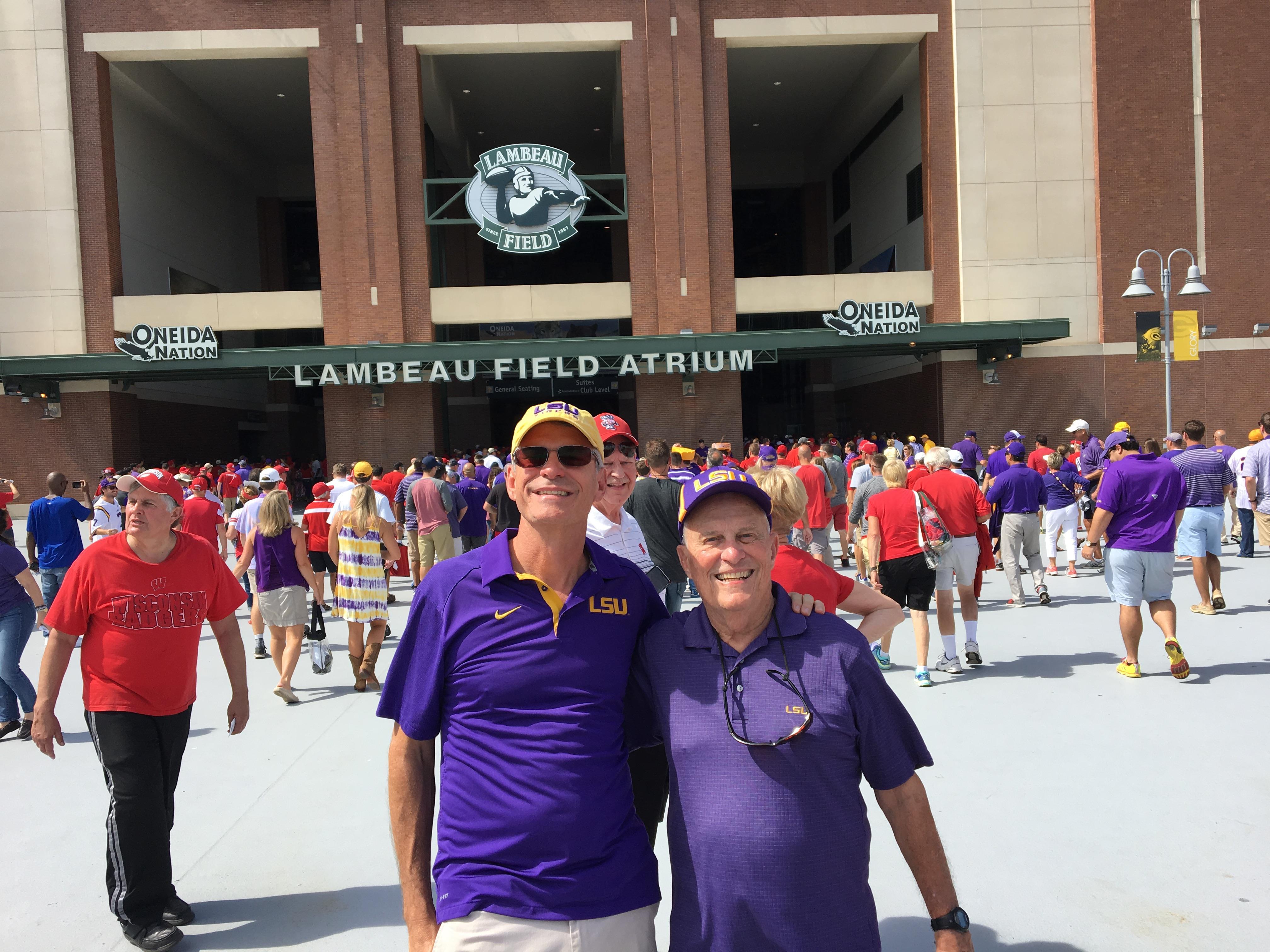 Two men in purple shirts and hats standing in front of a stadium