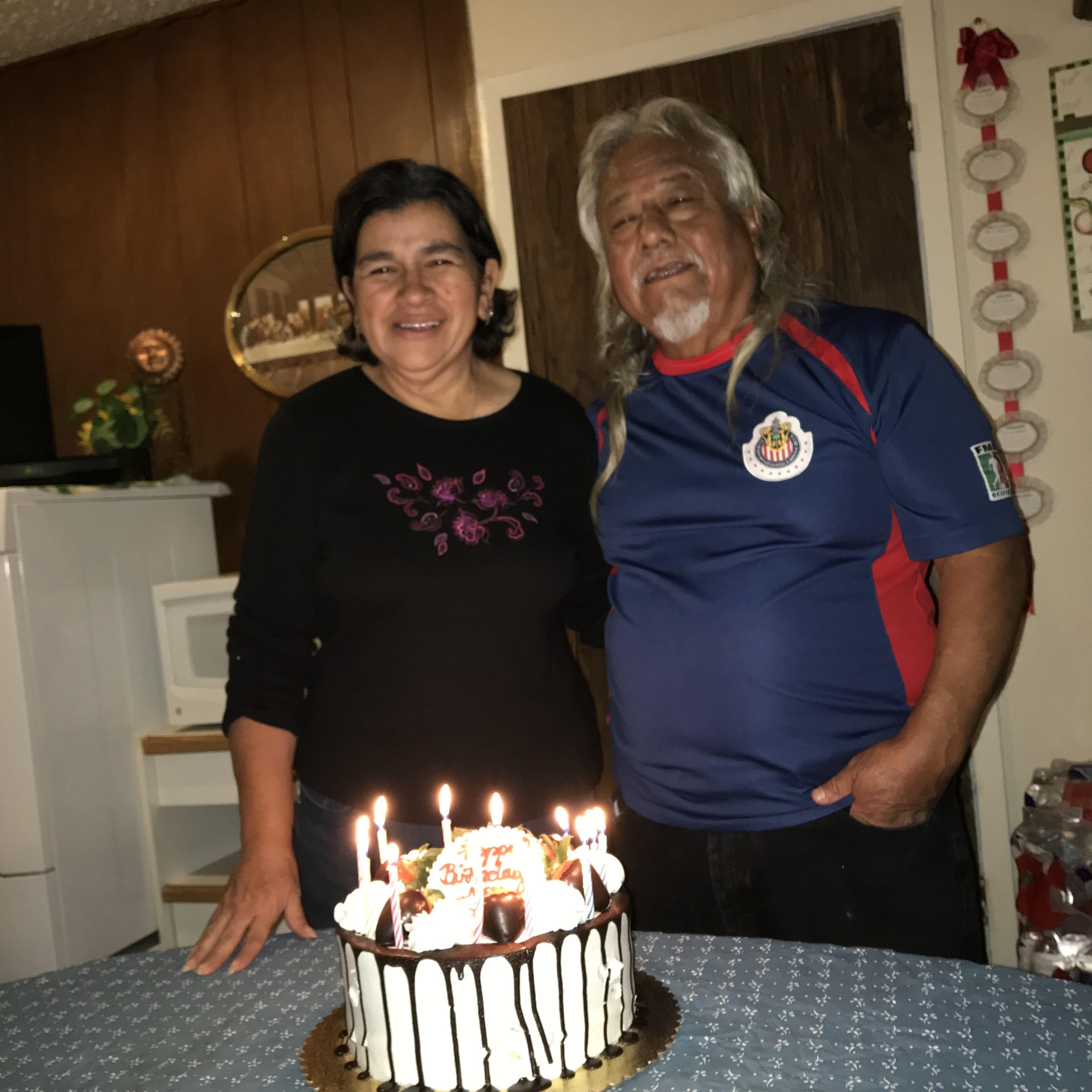 A man and woman standing next to a cake with lit candles
