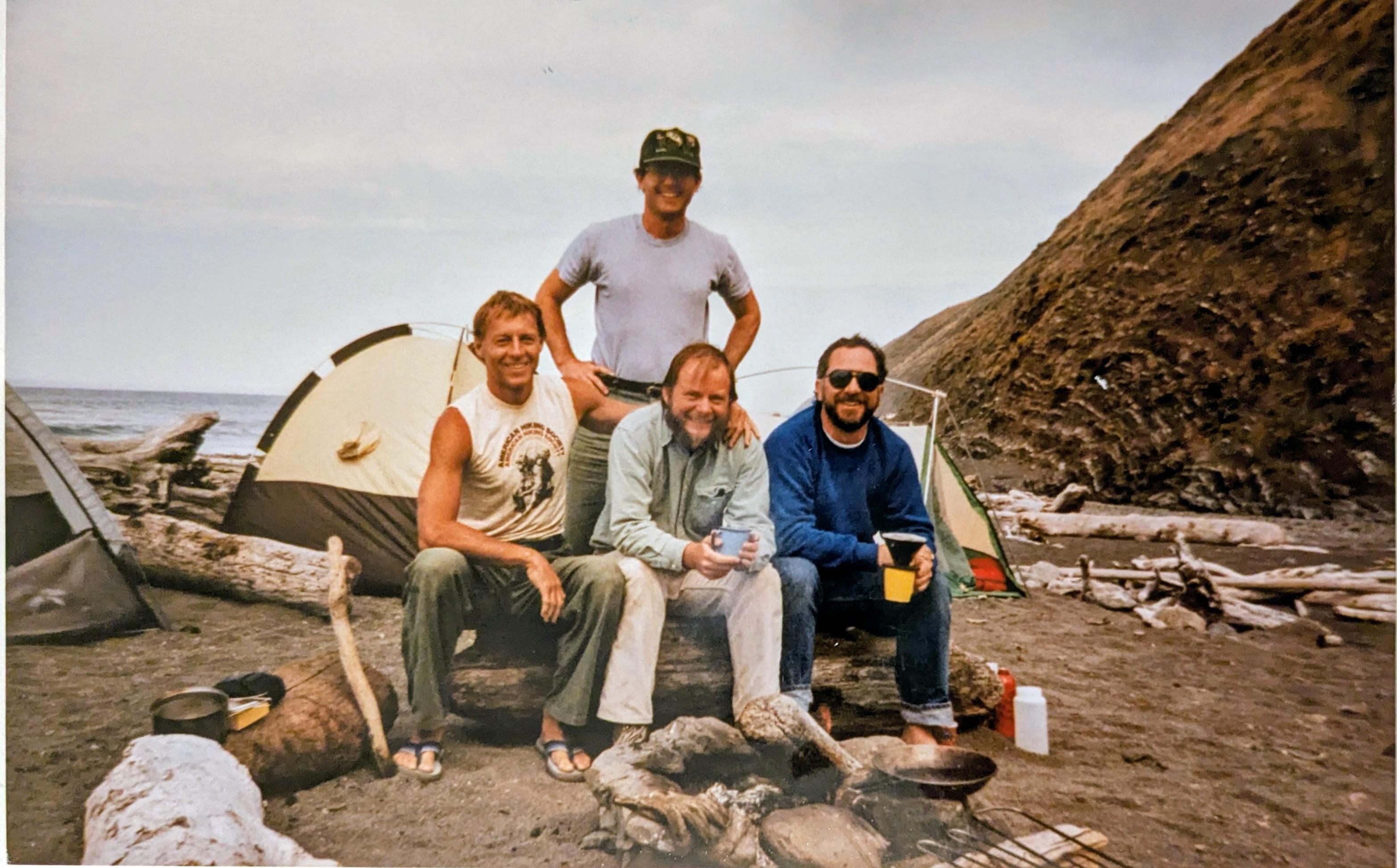 A group of men sitting on a log in front of a tent
