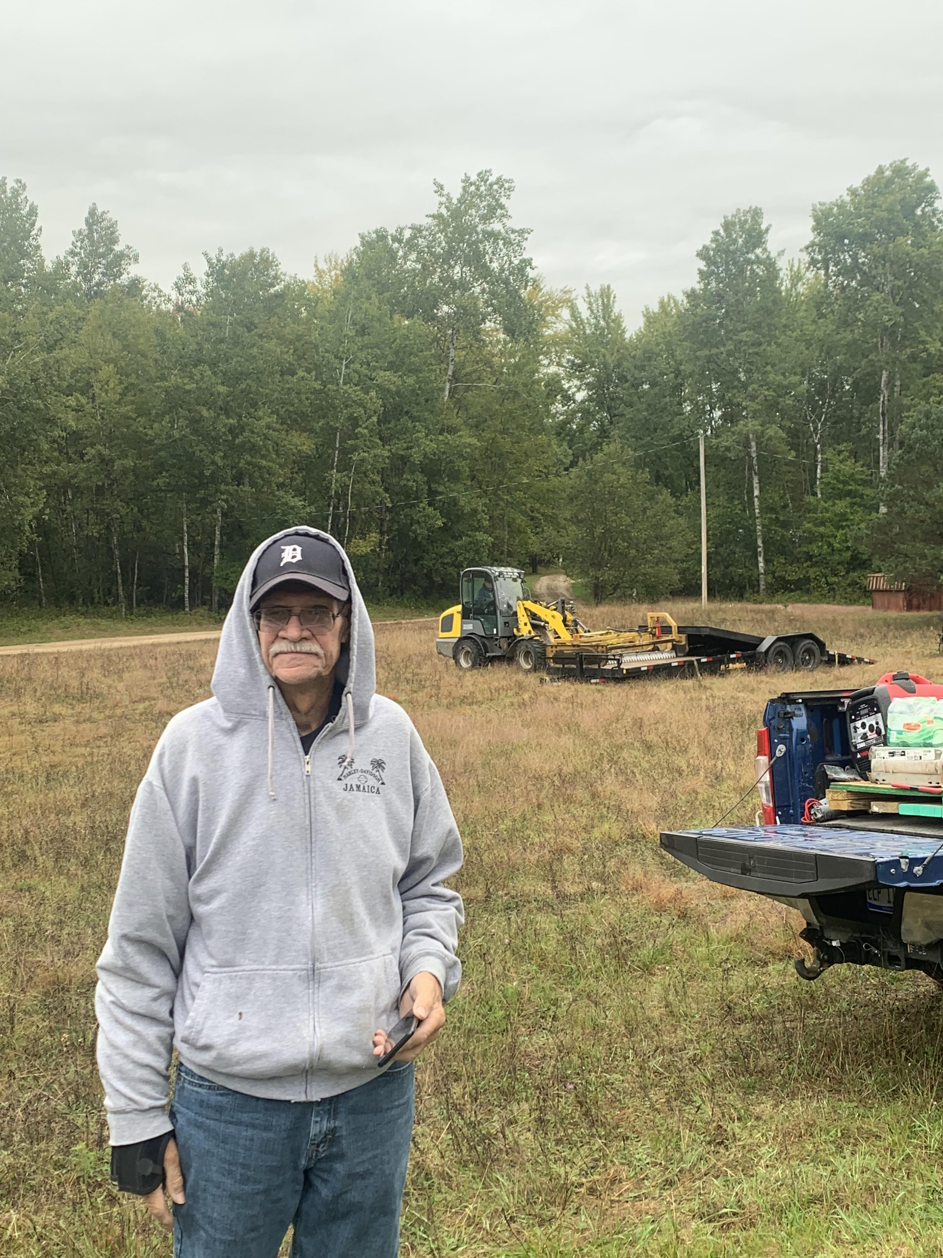 A man standing in a field with a tractor and a truck