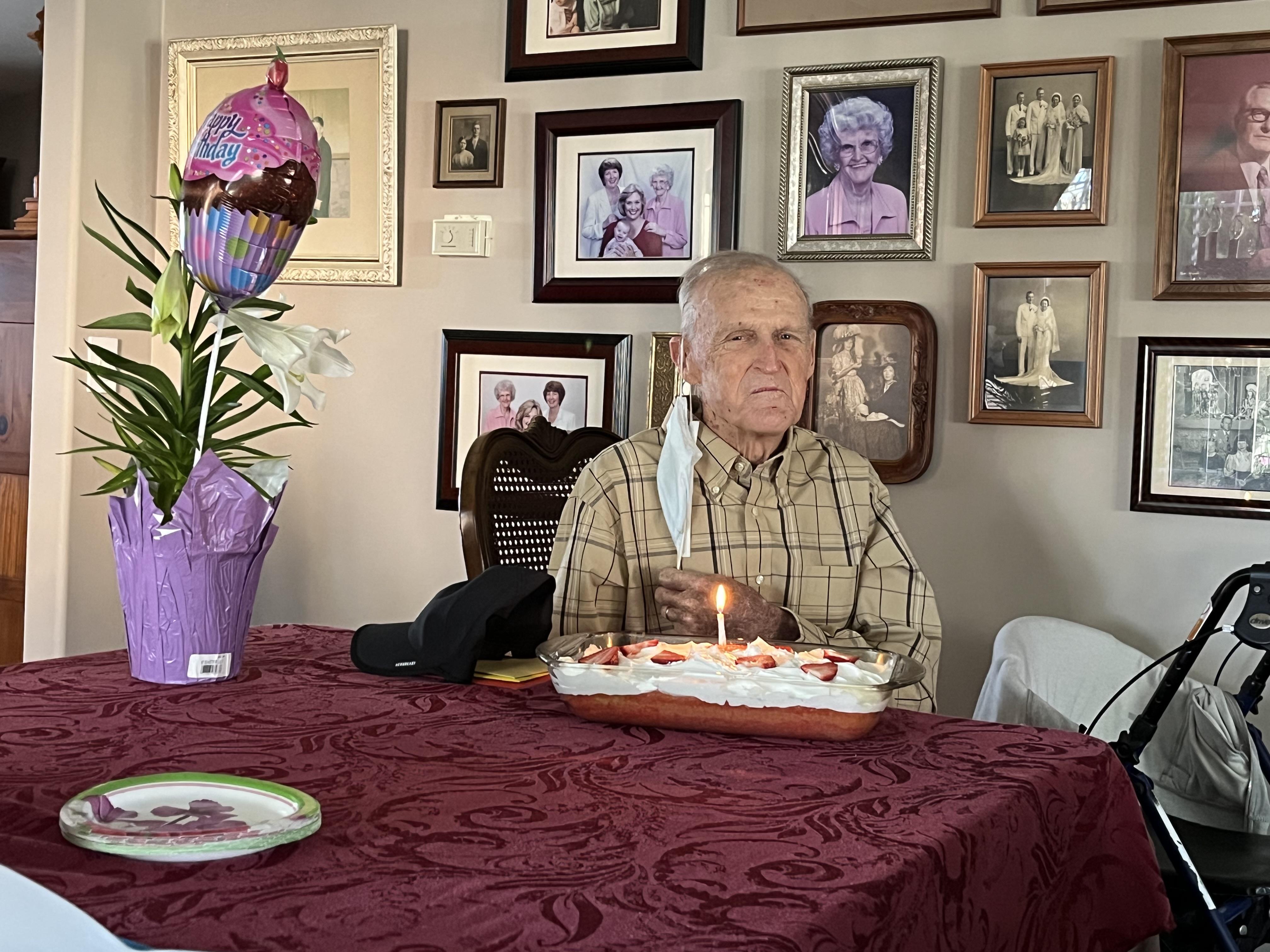 An old man sitting at a table with a cake and a balloon