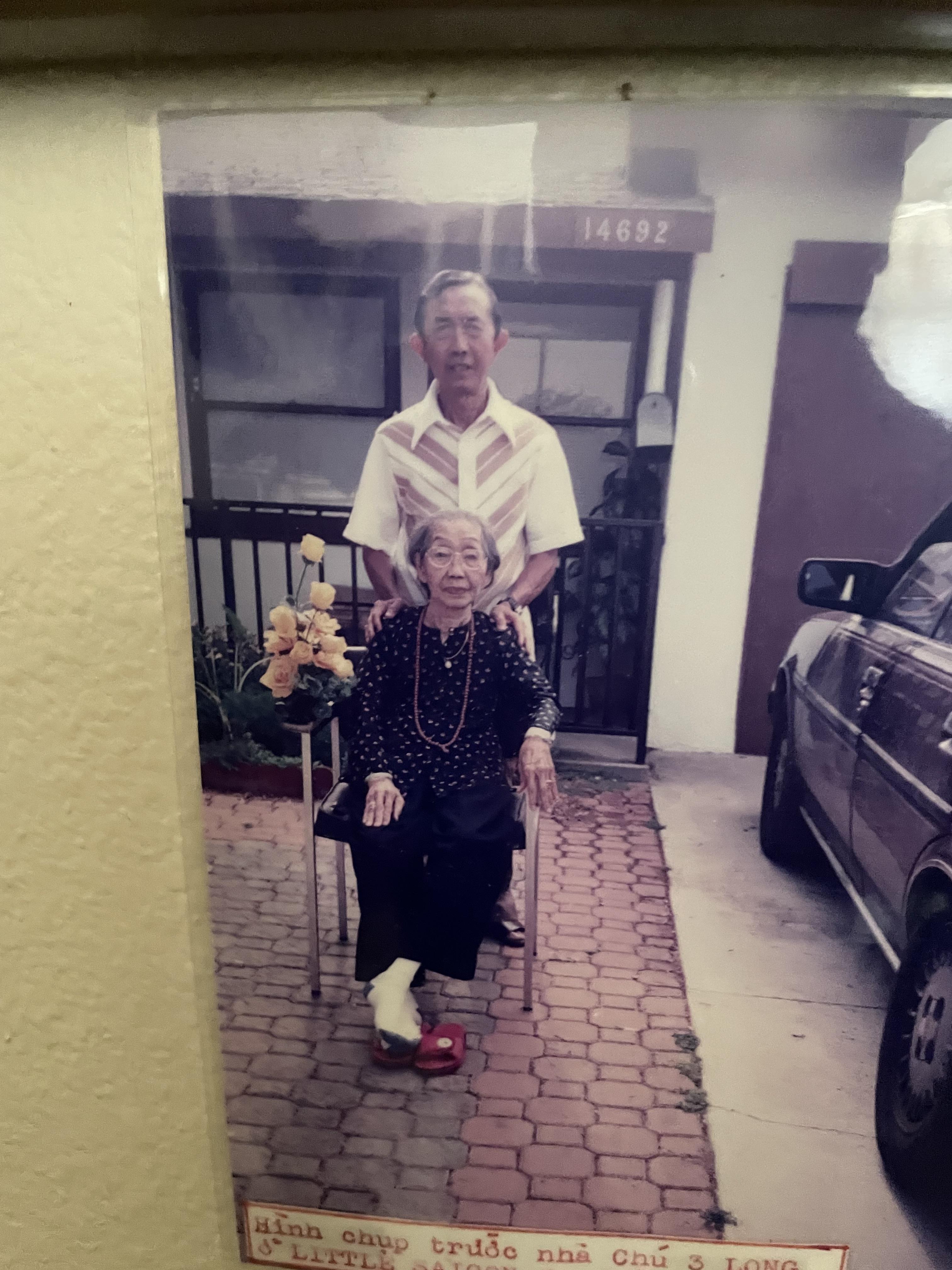 An elderly woman sitting in a chair with a man standing behind her