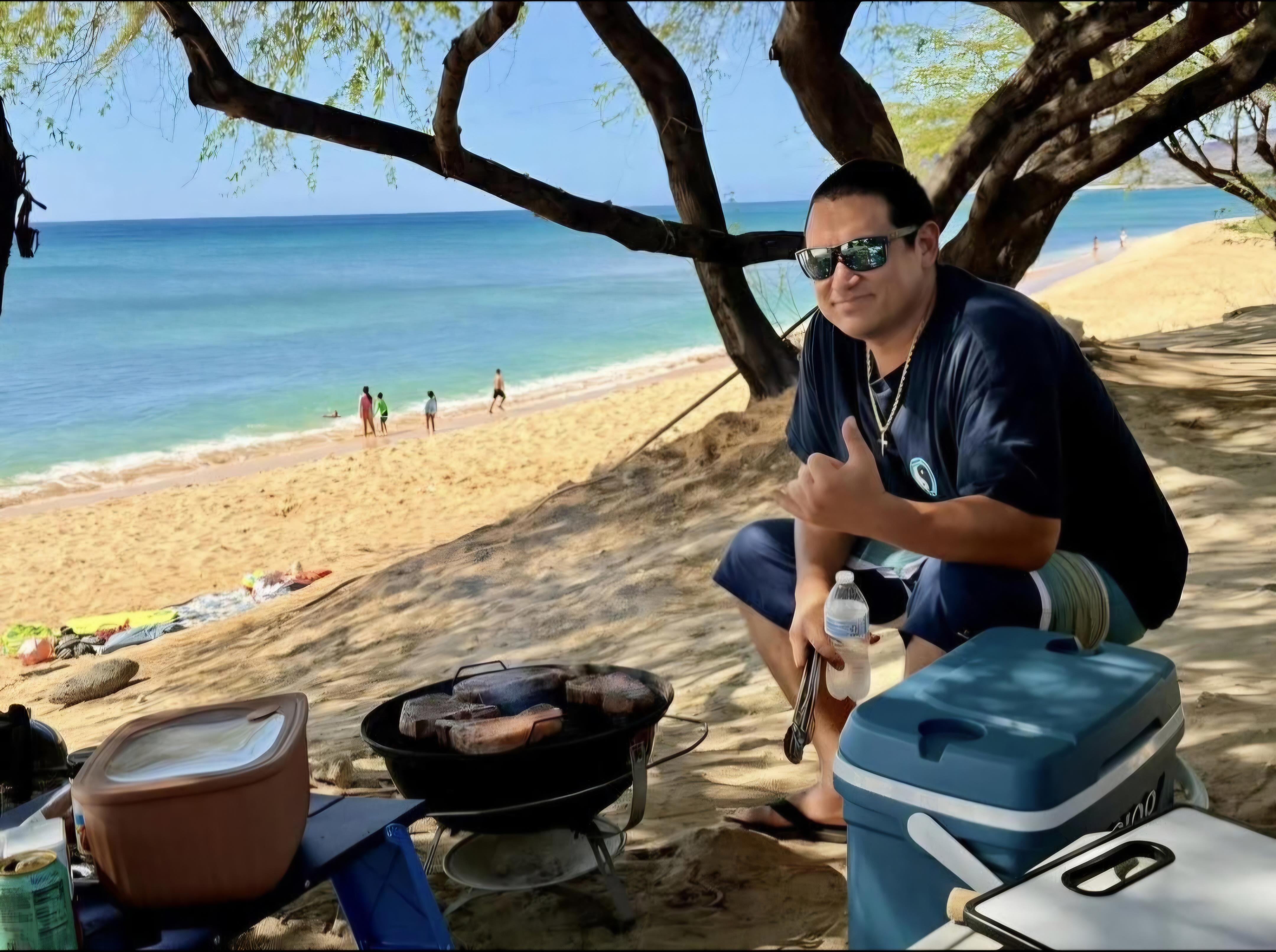 A man sitting on a beach with a barbecue grill