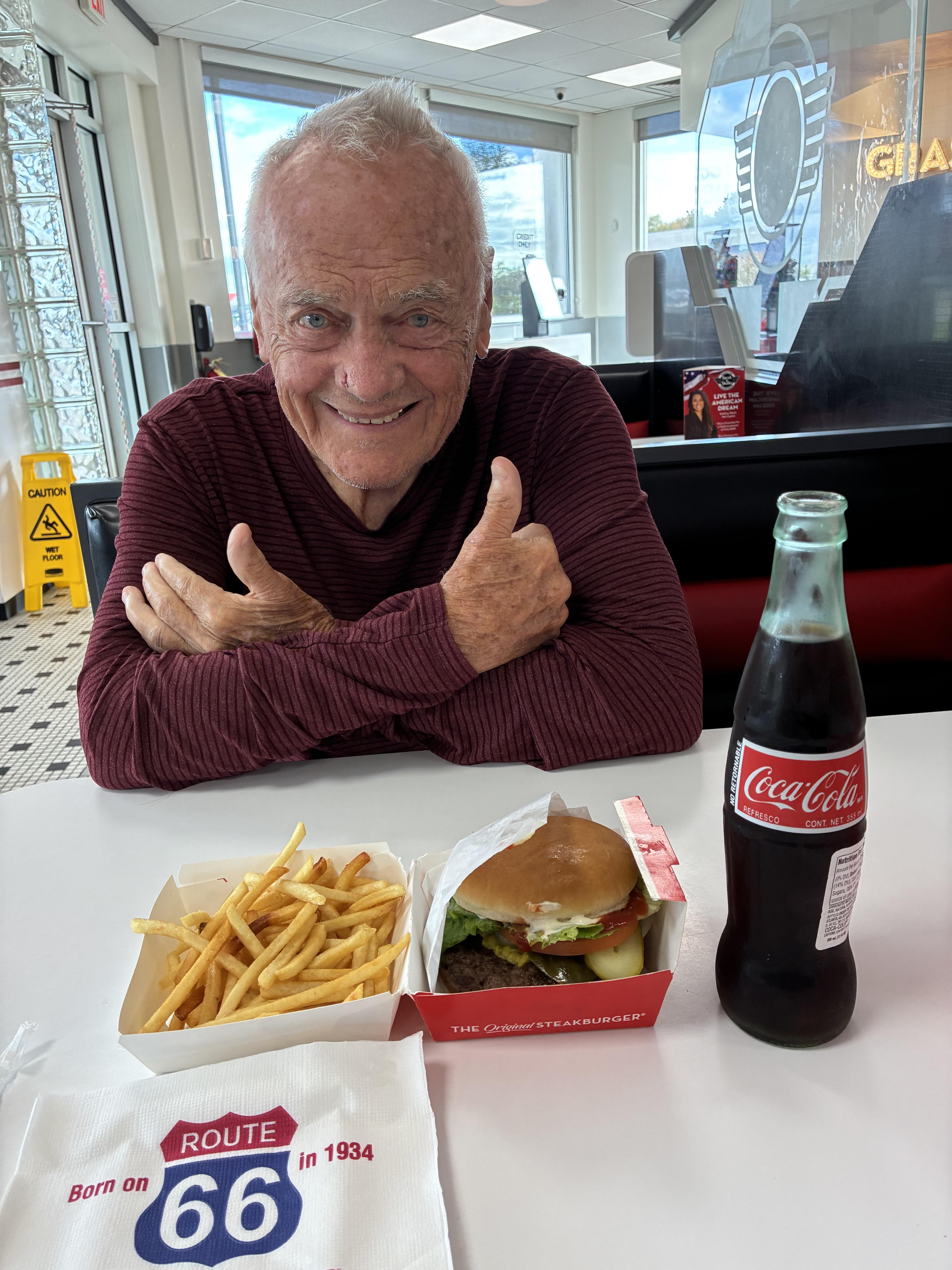 A man sitting at a table with a burger and fries