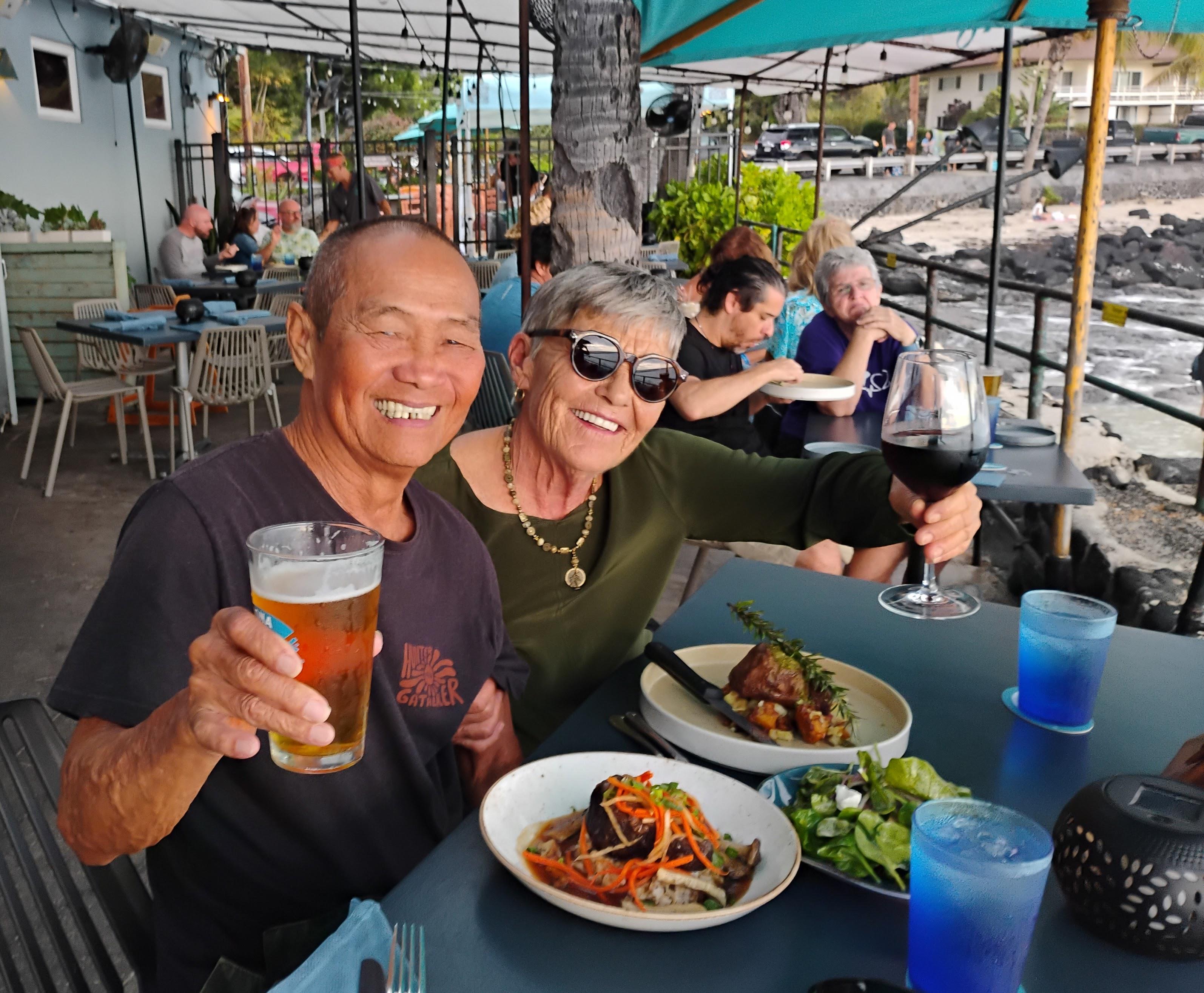 A man and woman sitting at a table with food and drinks