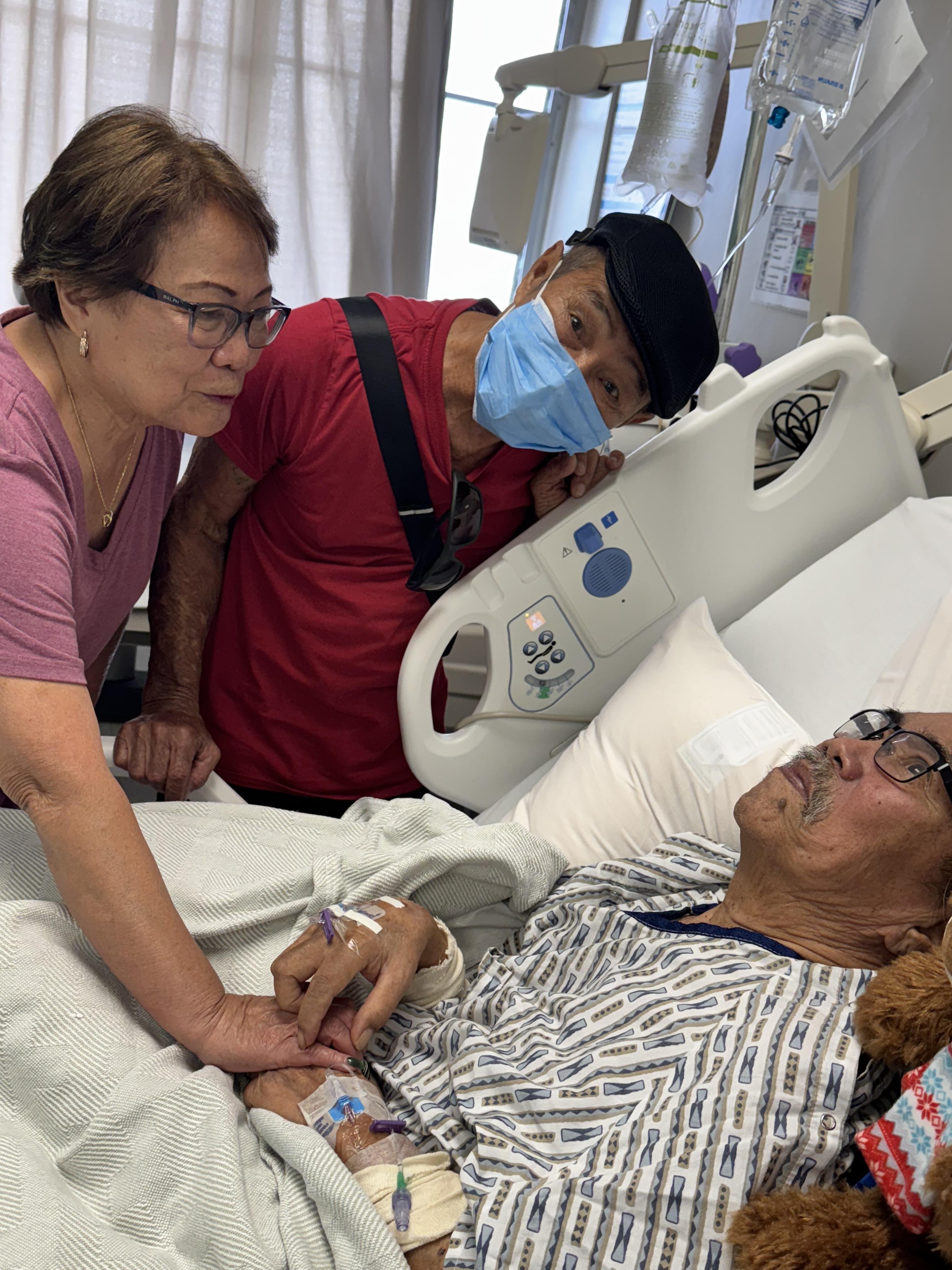 A man lying in a hospital bed with a woman and a man in a mask
