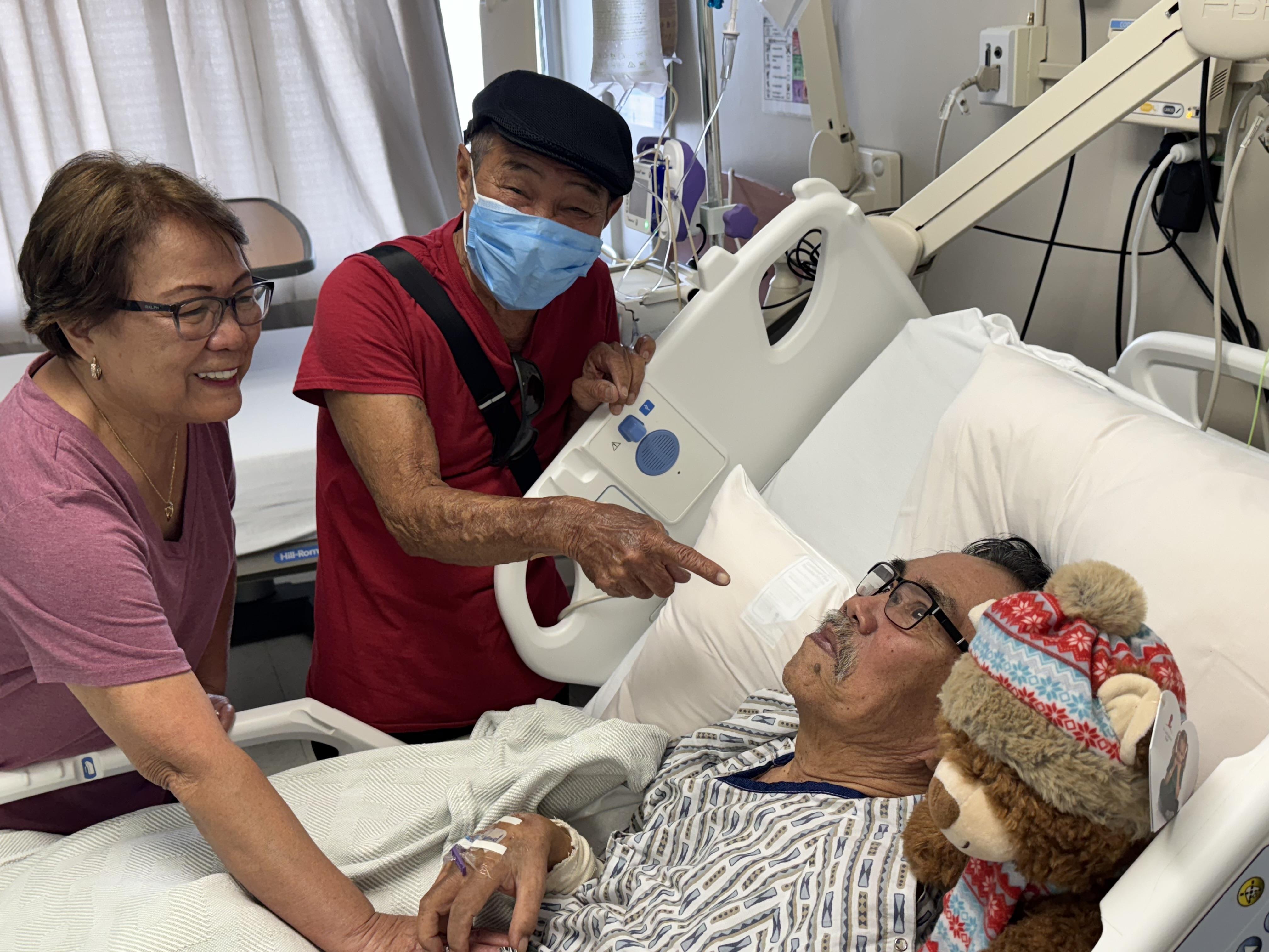A man lying in a hospital bed with a woman pointing at him