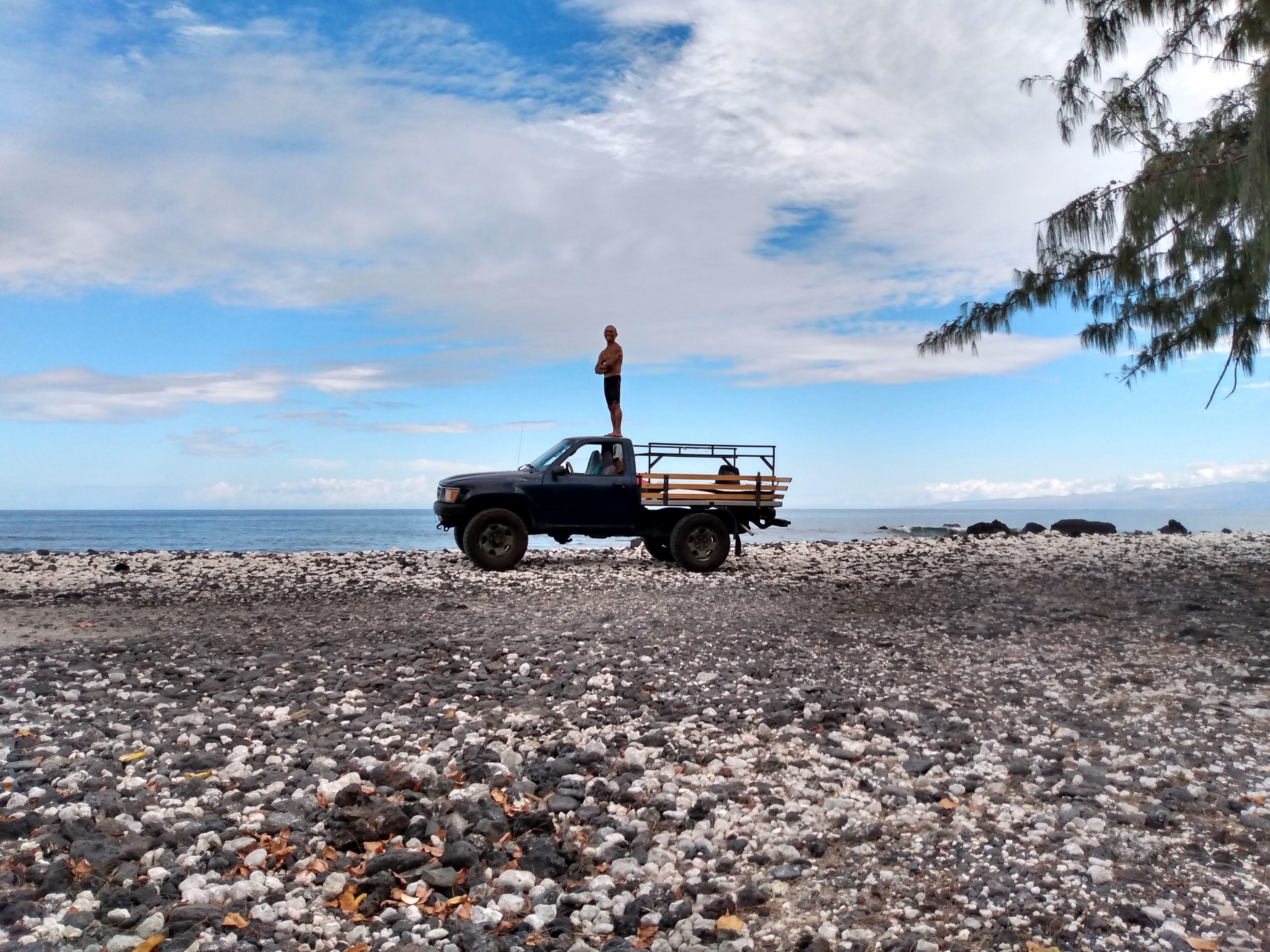 A person standing on the top of a truck on a rocky beach