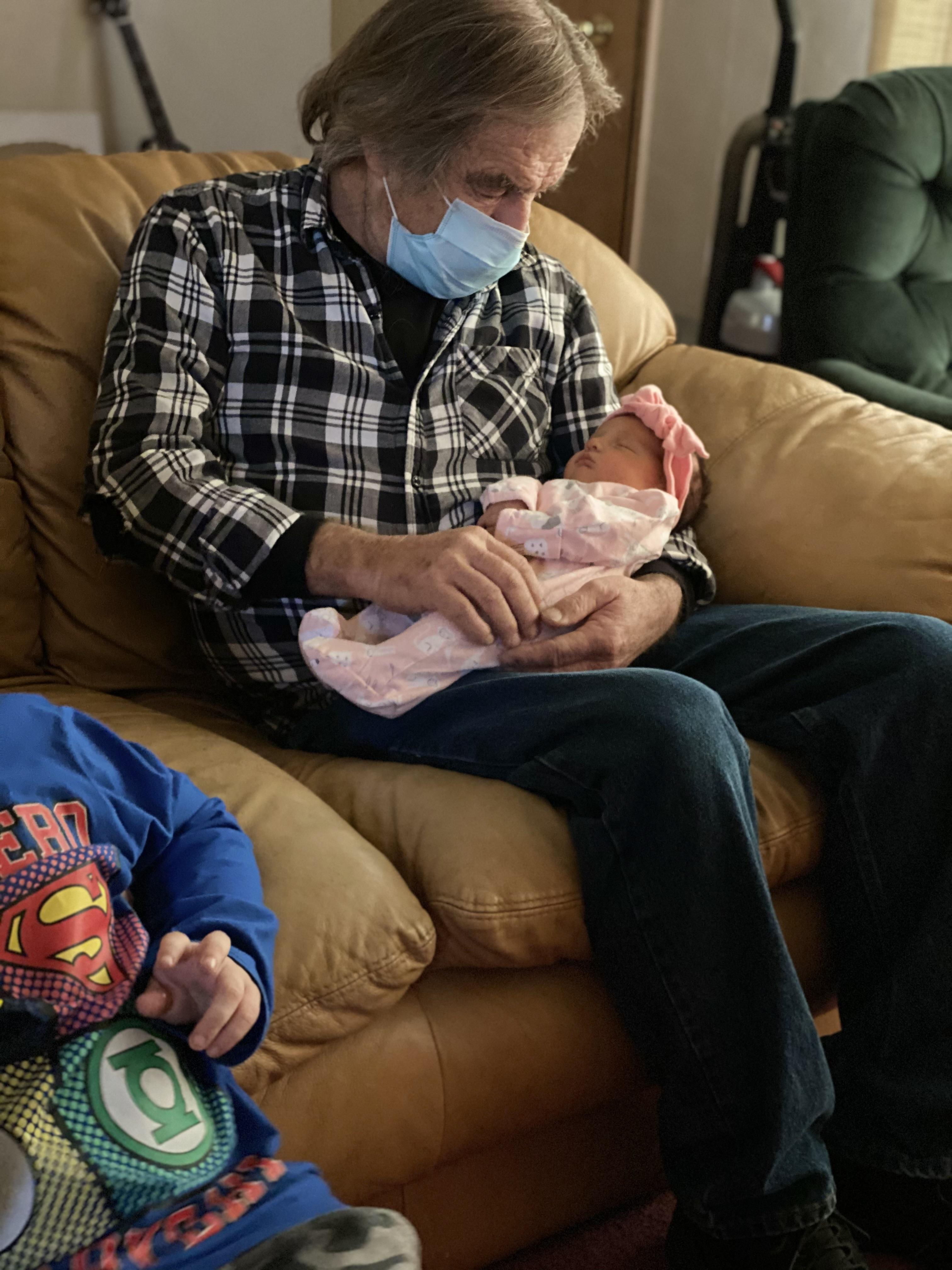 An old man wearing a face mask holding a baby