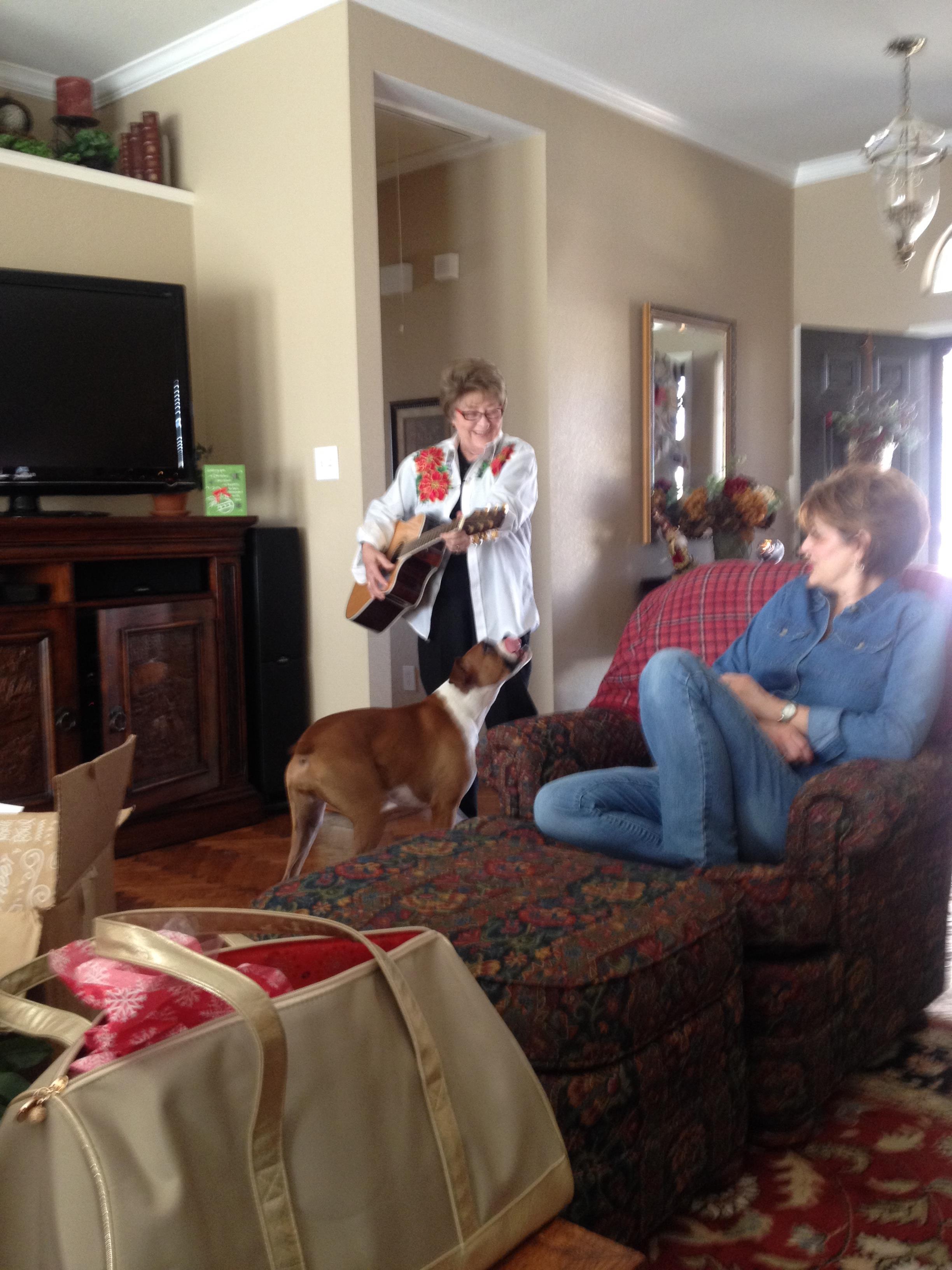 A woman playing guitar with a dog in a living room