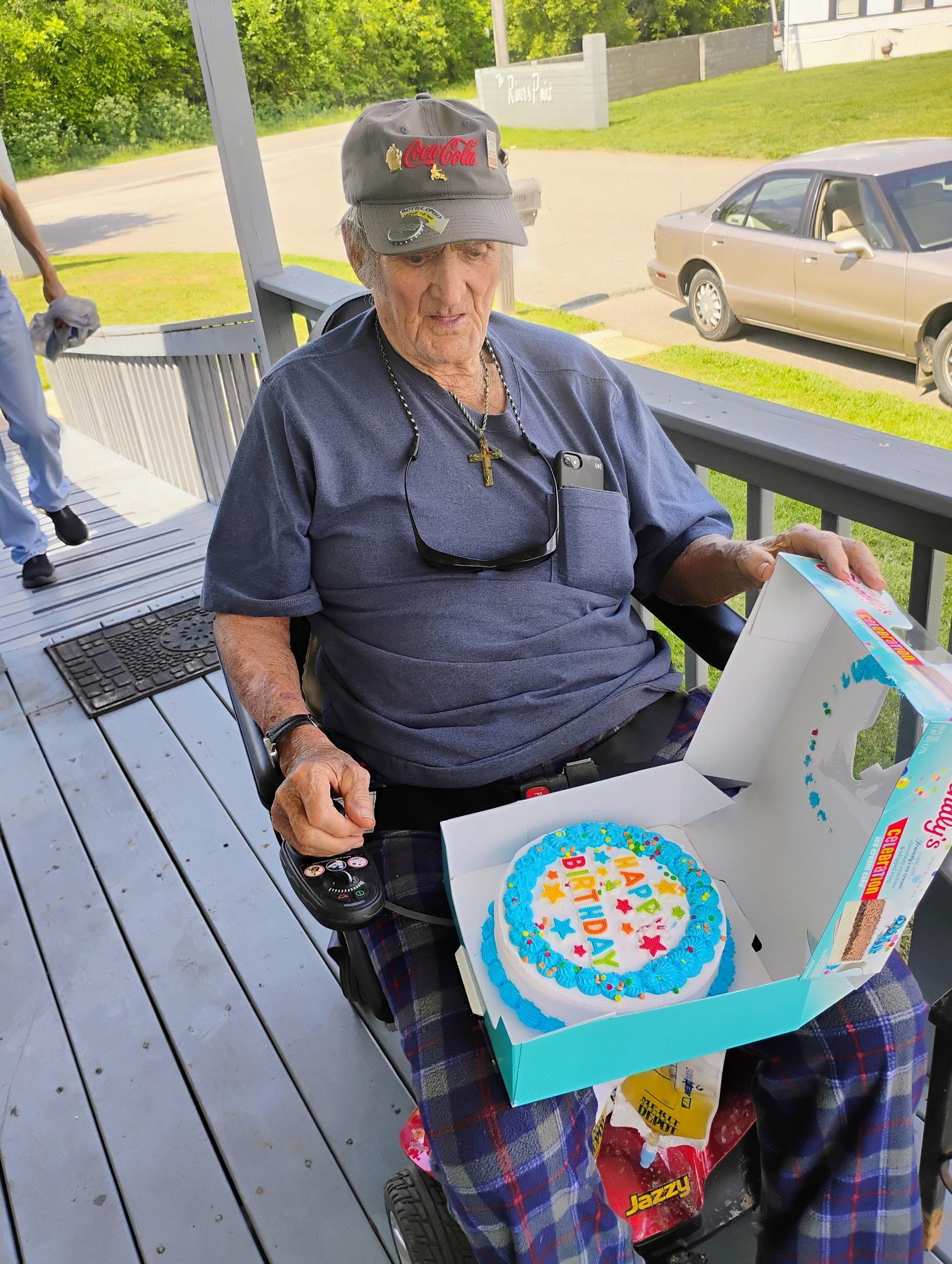 An old man sitting on a porch with a cake