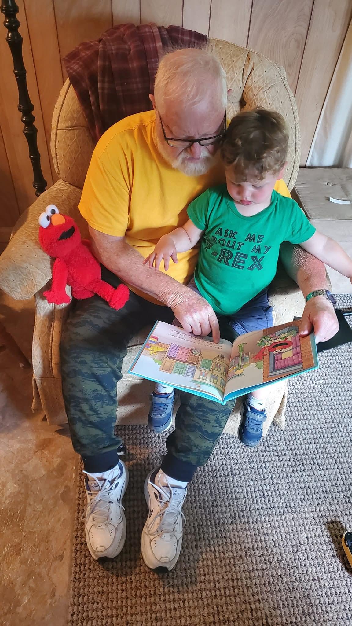An old man and a young boy sitting in a chair reading a book