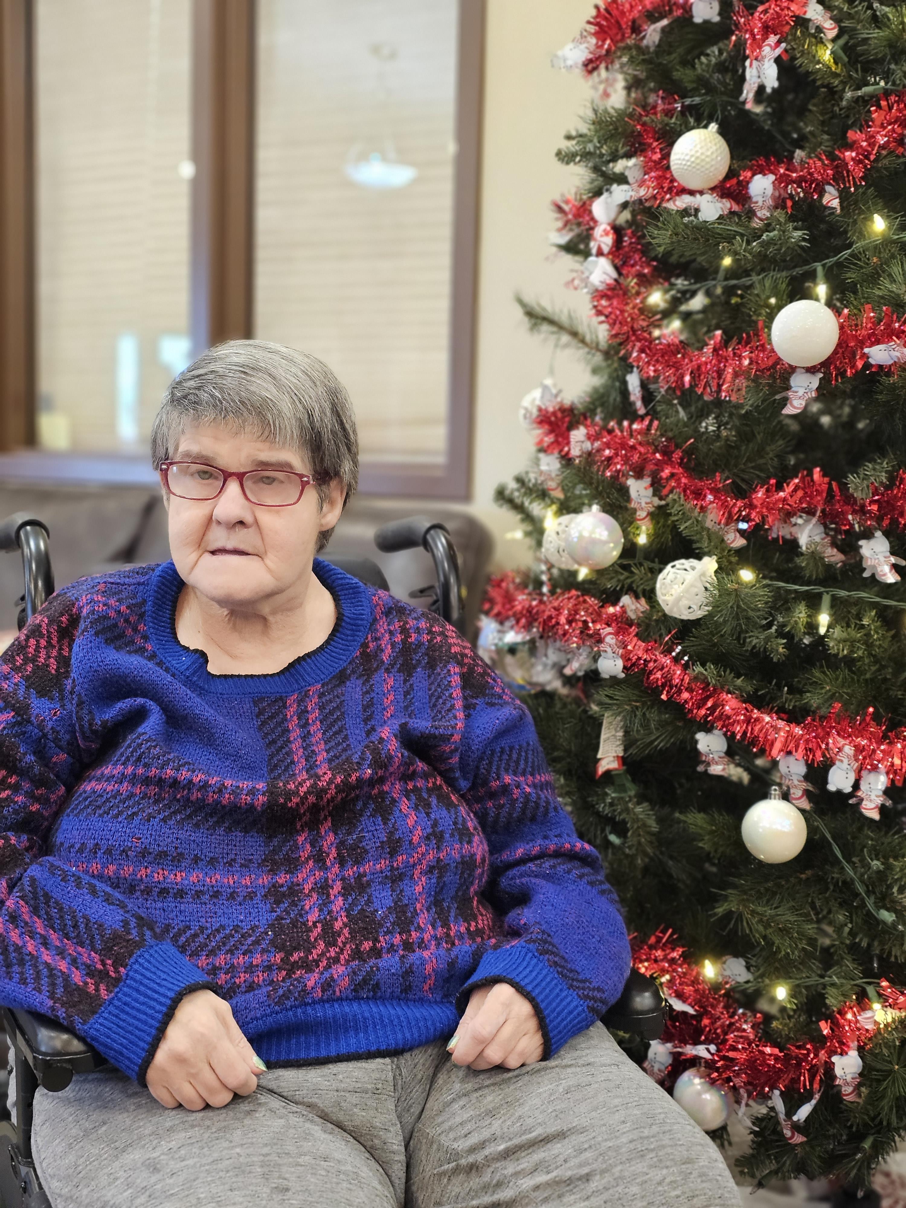 A woman sitting in a wheelchair next to a christmas tree
