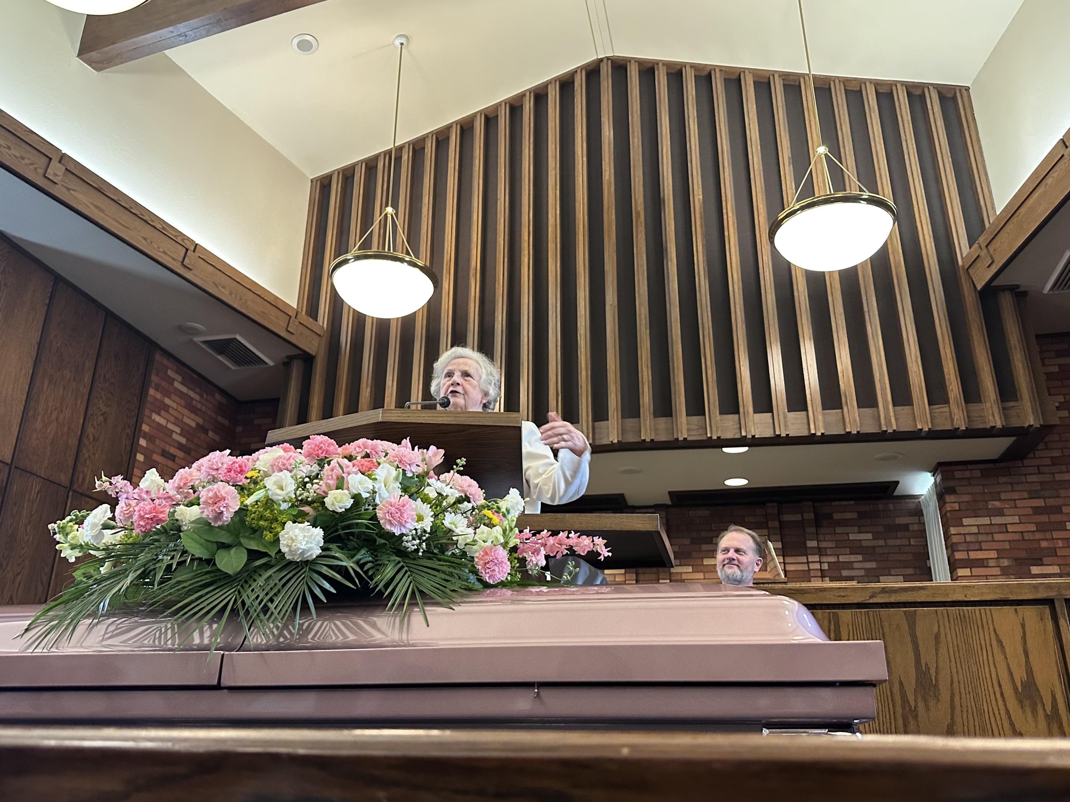 A man standing at a podium with a coffin and flowers