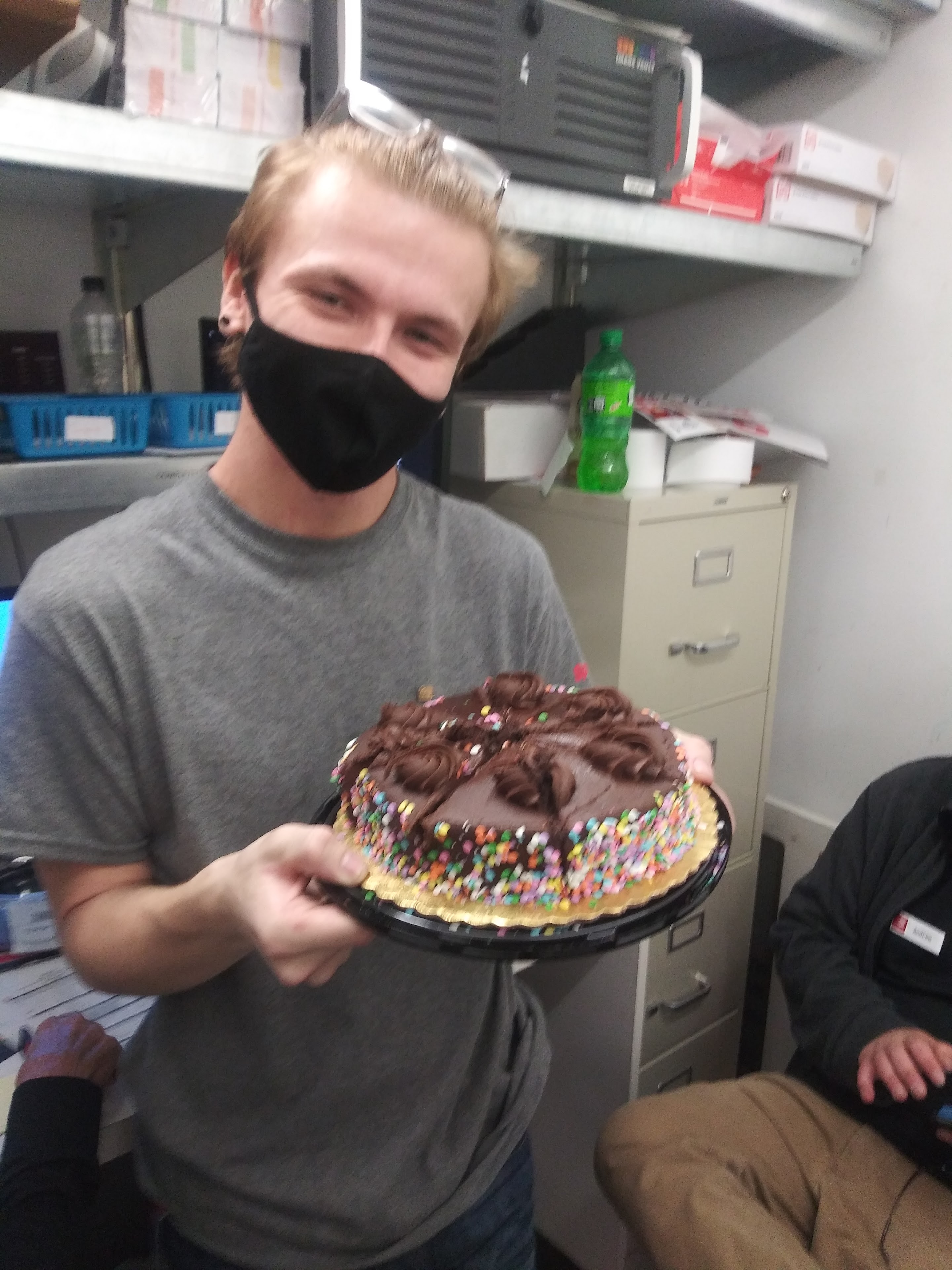 A man wearing a face mask holding a cake