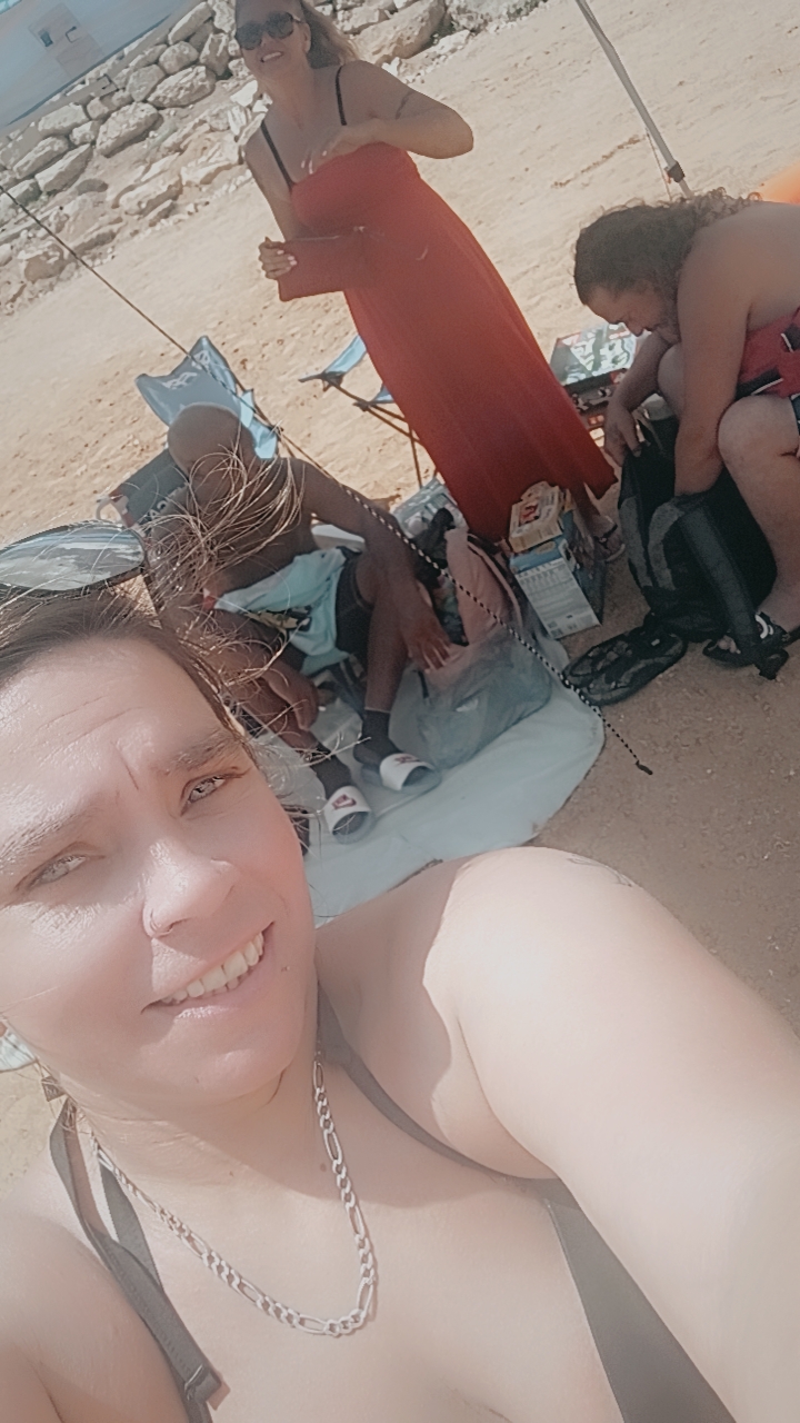 A selfie of a woman with a group of people sitting on a beach