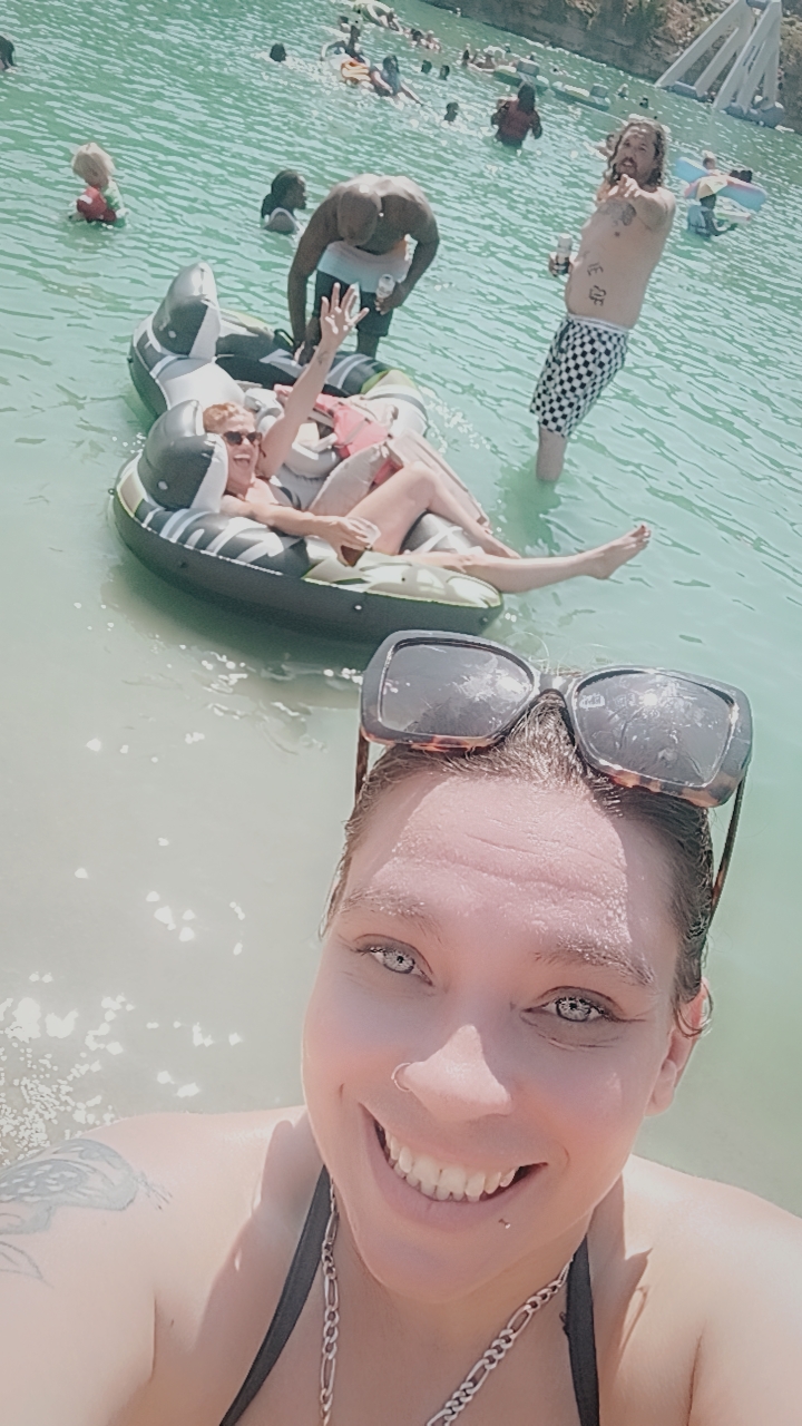 A selfie of a woman in a body of water with people in the background