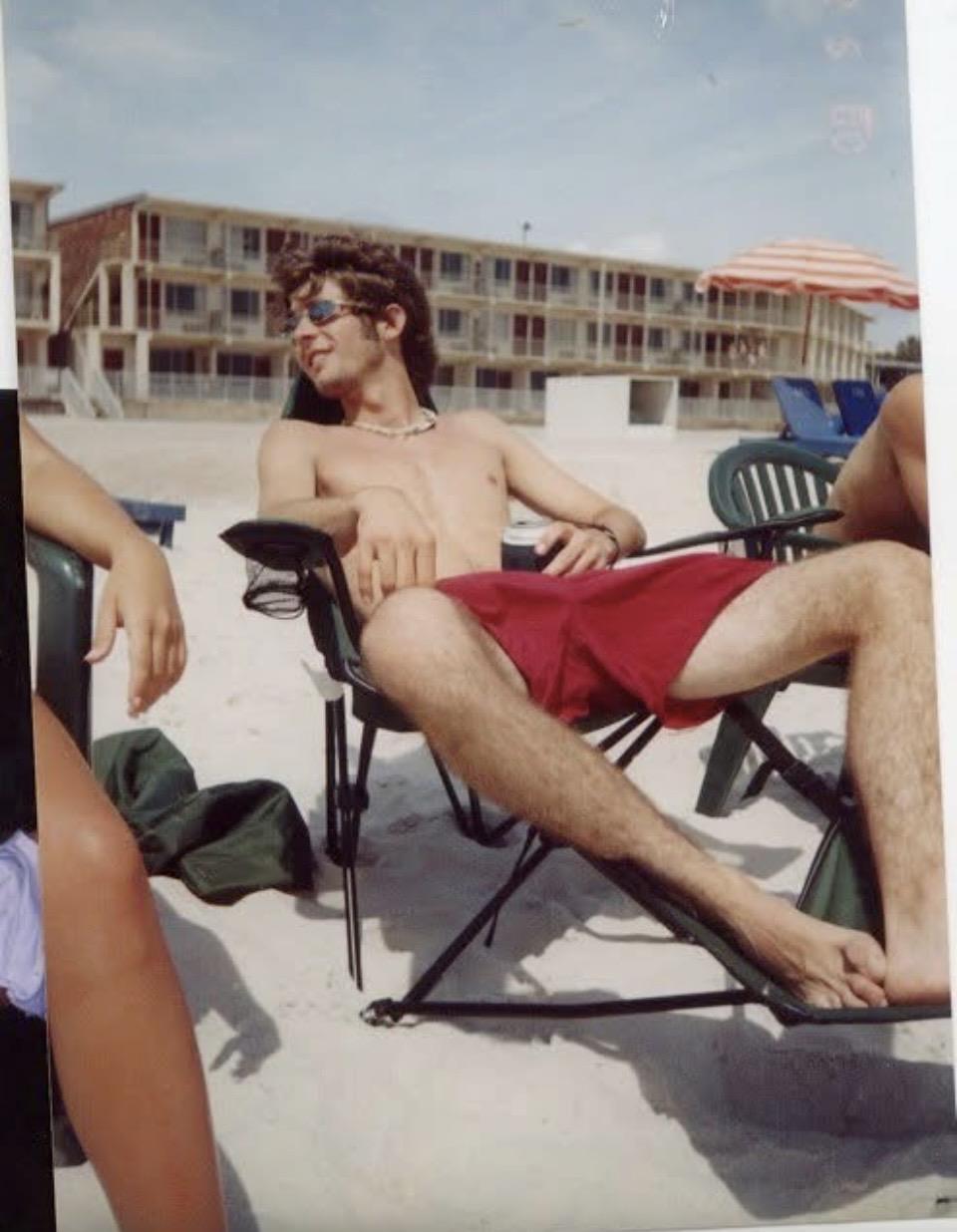A man in red shorts sitting in a chair on a beach