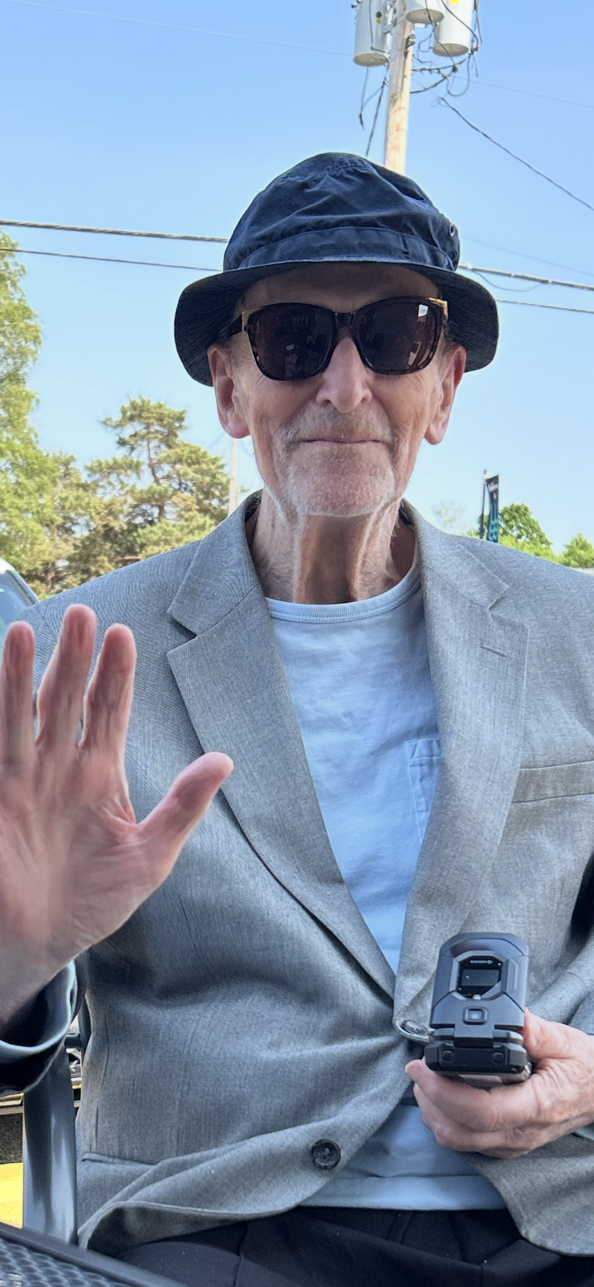 A man wearing sunglasses and a hat waving