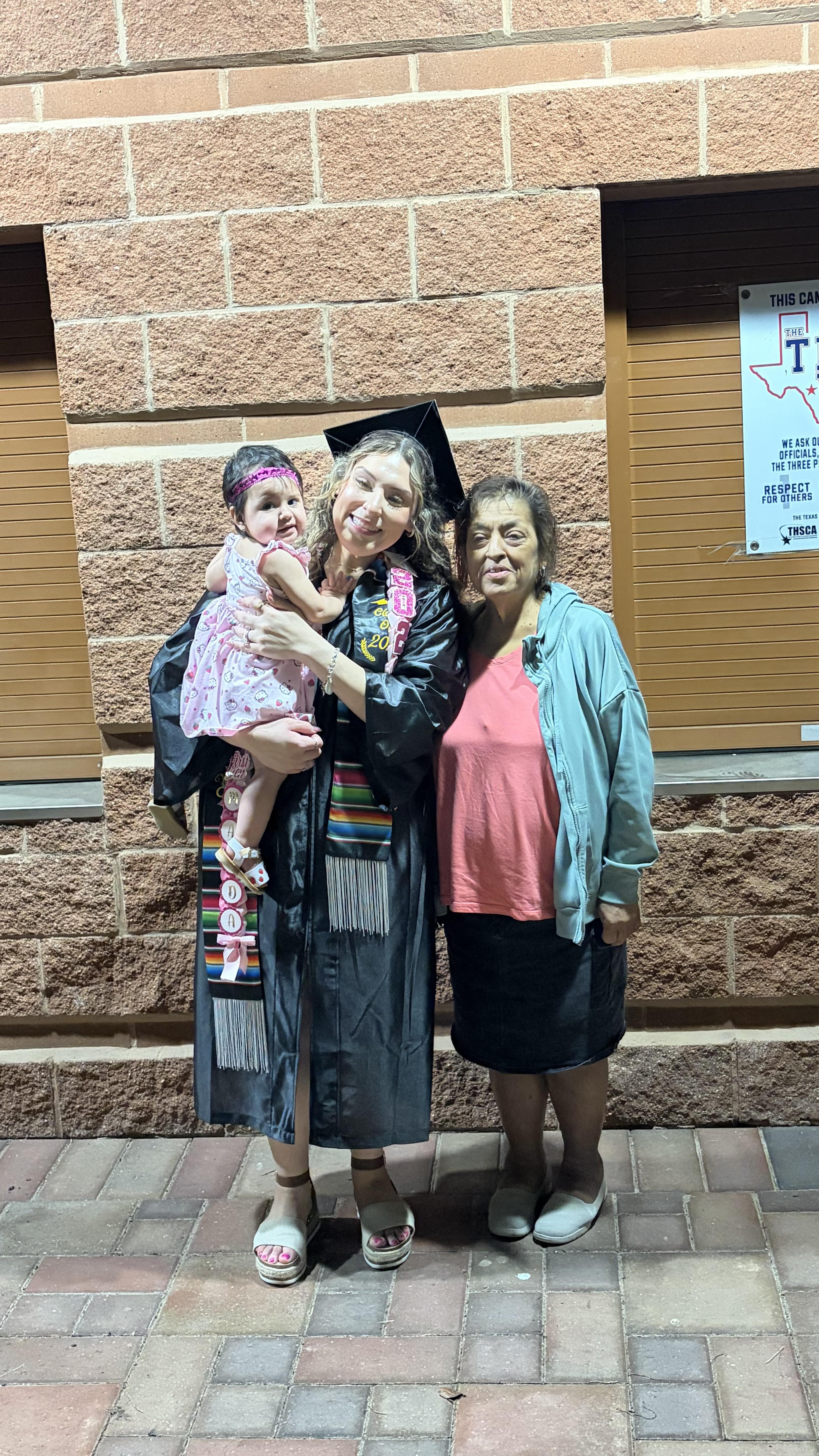 A woman in a graduation gown and cap with a baby and a woman in a hat