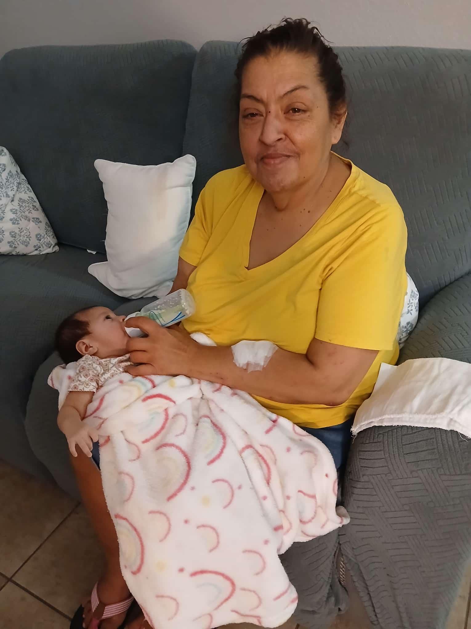 A woman sitting on a couch feeding a baby
