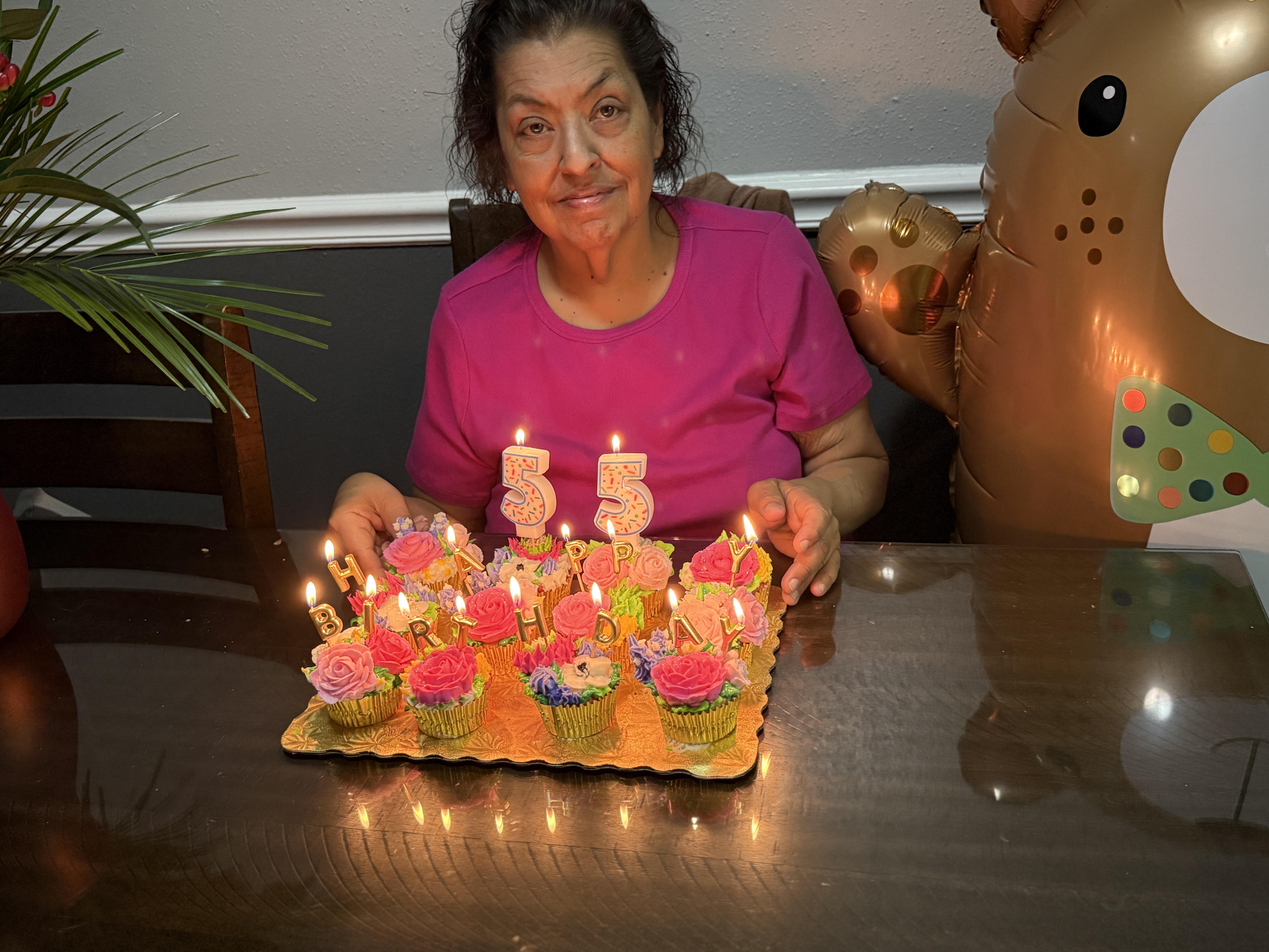 A woman sitting at a table with a tray of cupcakes and candles