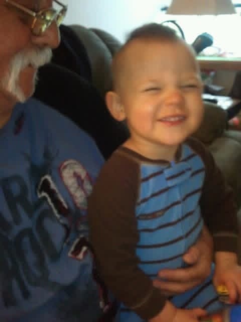 A baby smiling next to an old man