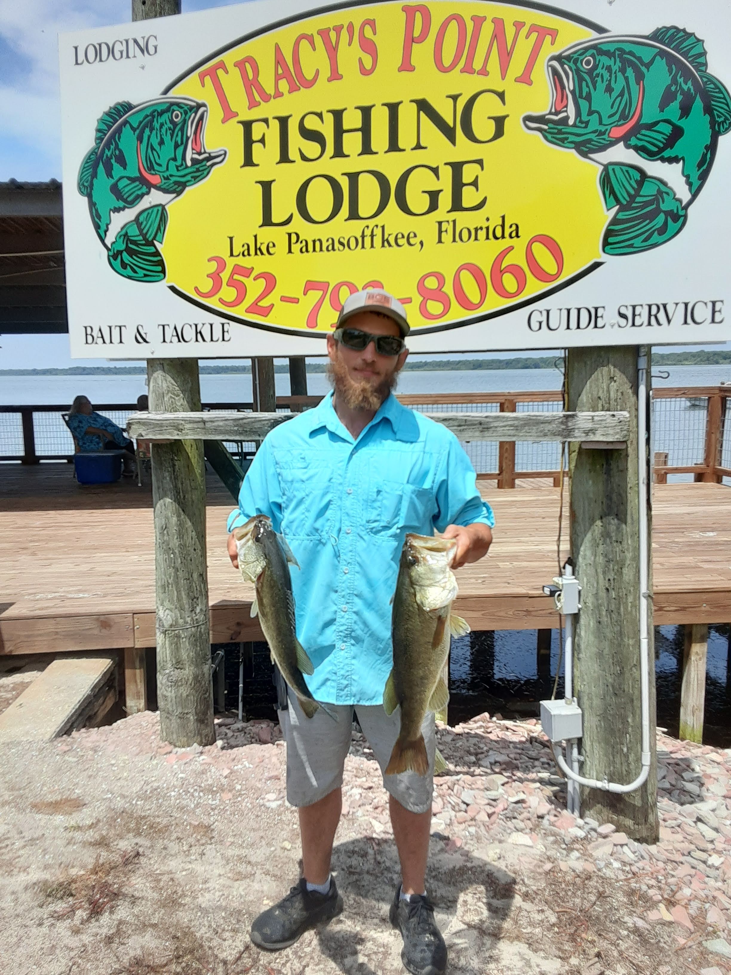 A man holding two fish in front of a sign