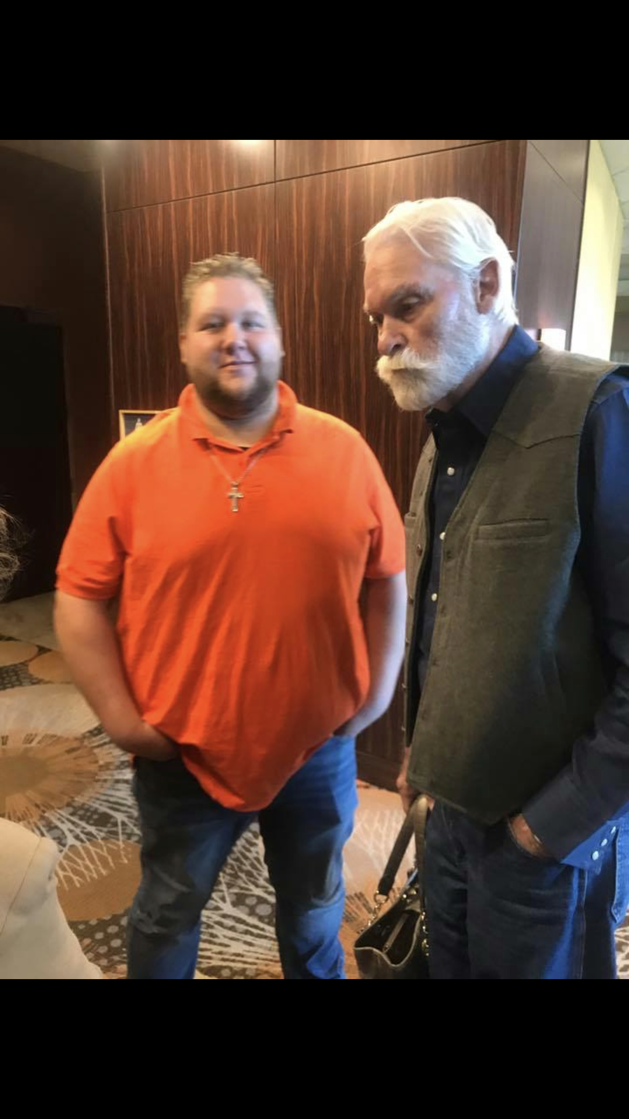 A man in an orange shirt standing next to another man in a room