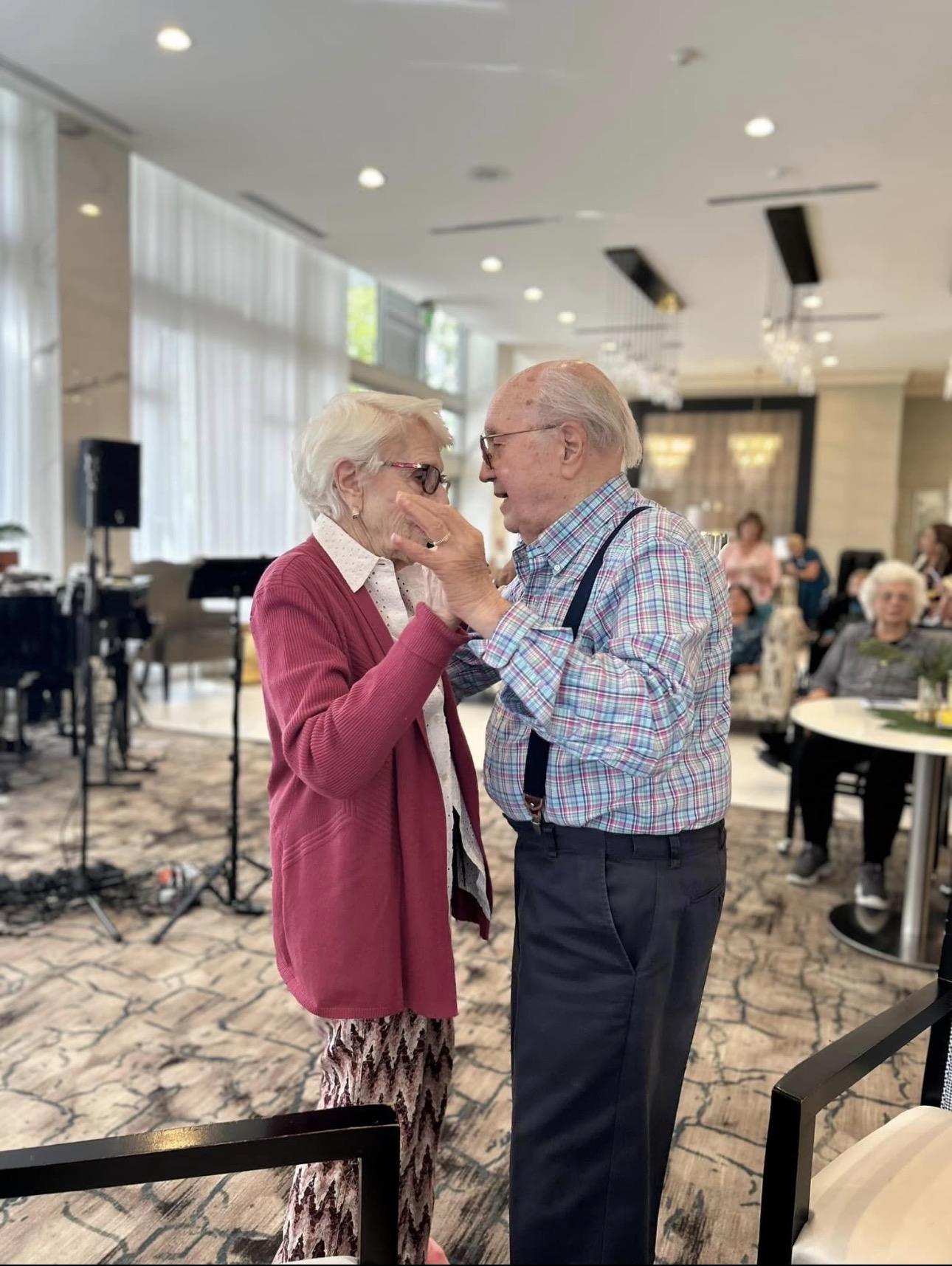 An older man and woman standing in a room with a group of people