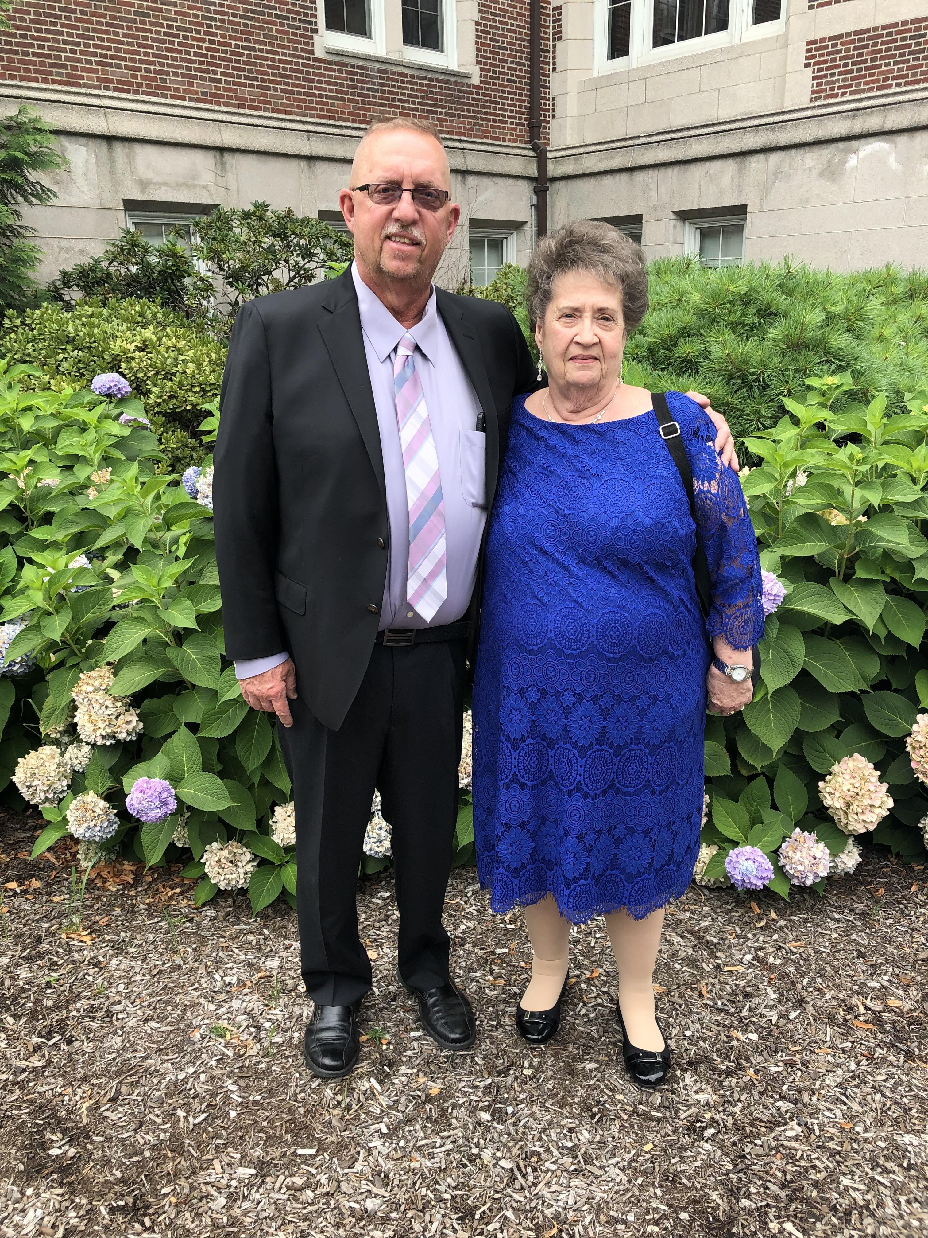 A man and woman standing together in front of bushes