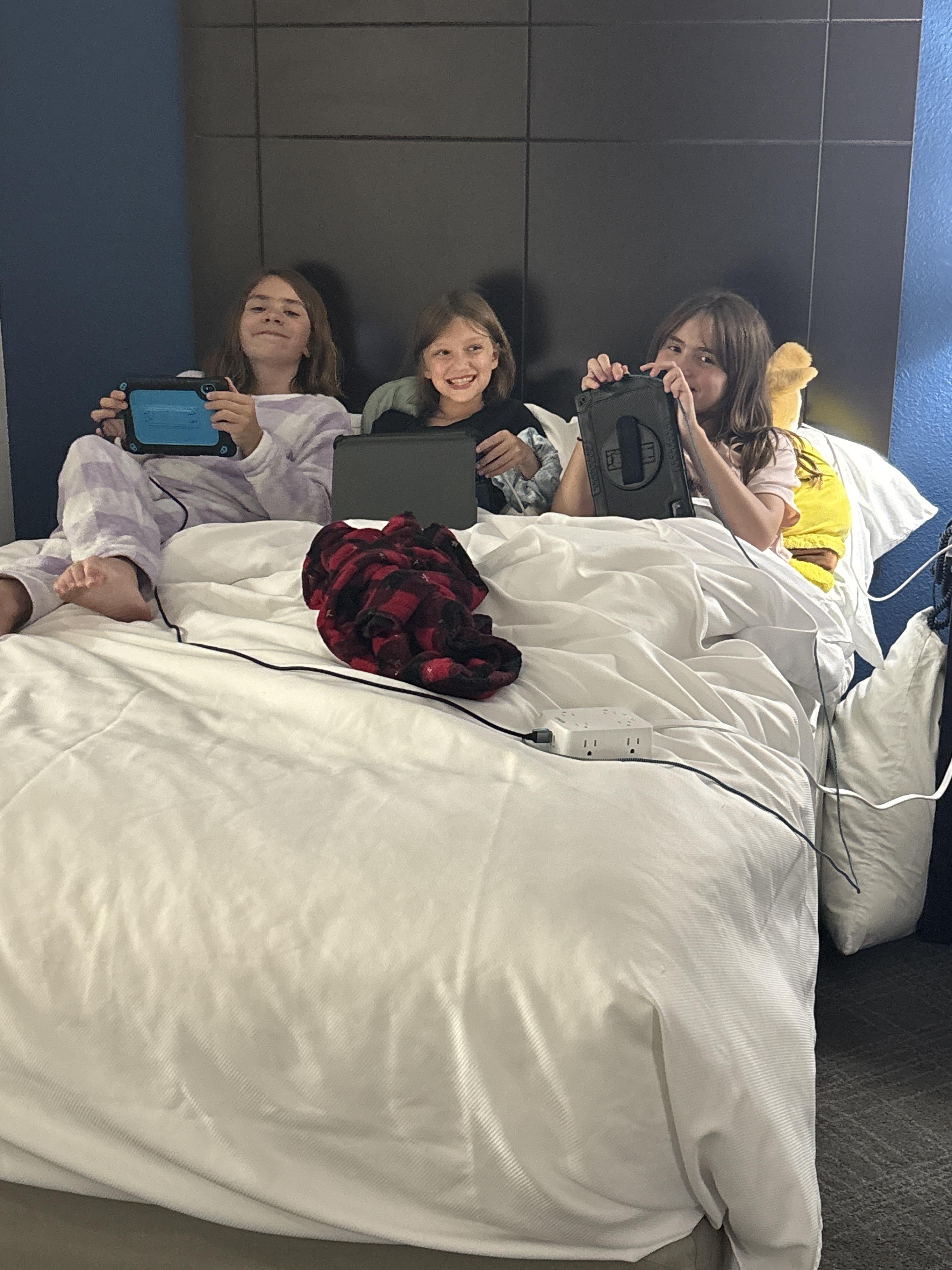 A group of girls sitting in bed with electronic devices