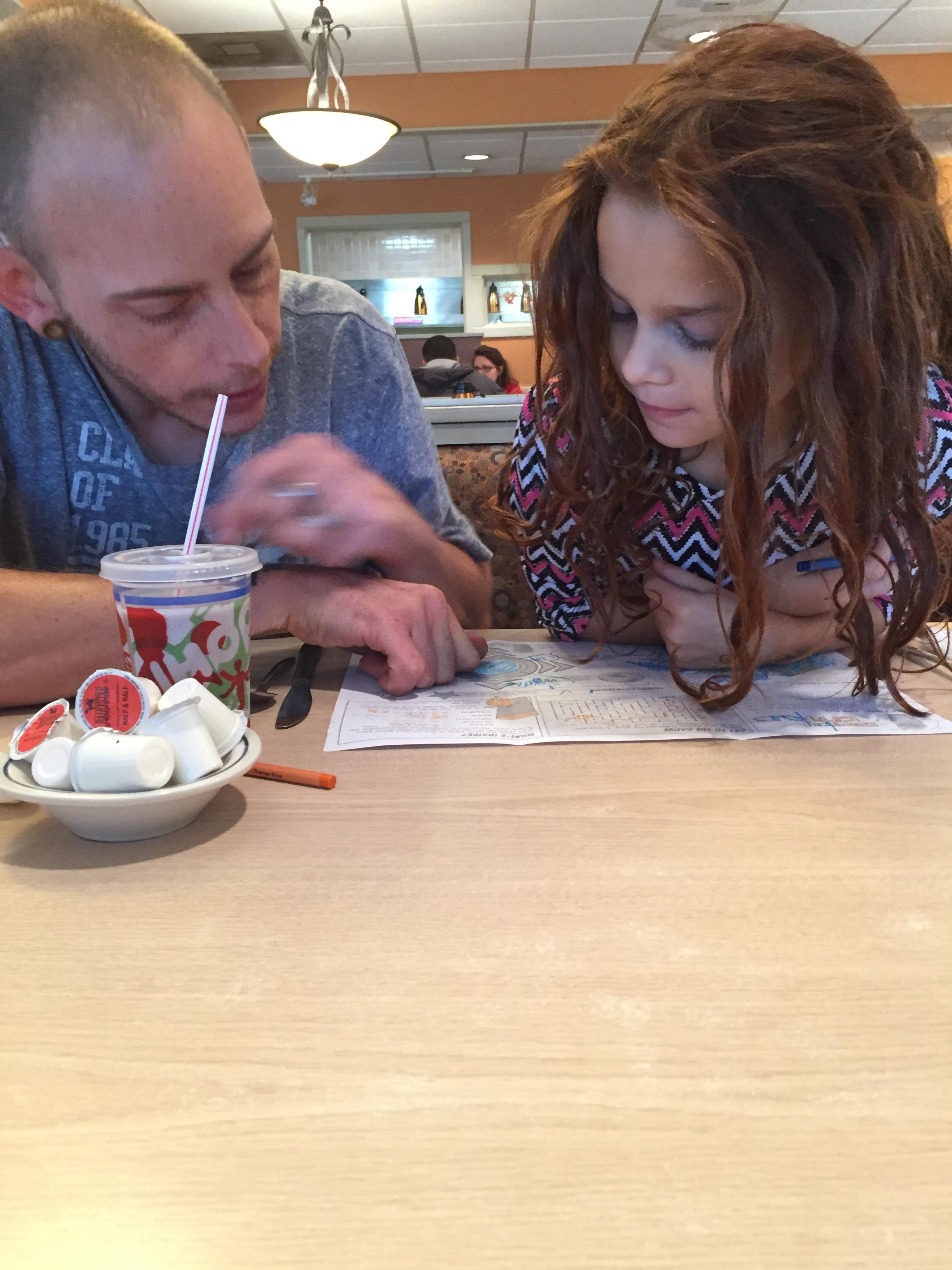 A man and a girl looking at a paper and drinking from a cup
