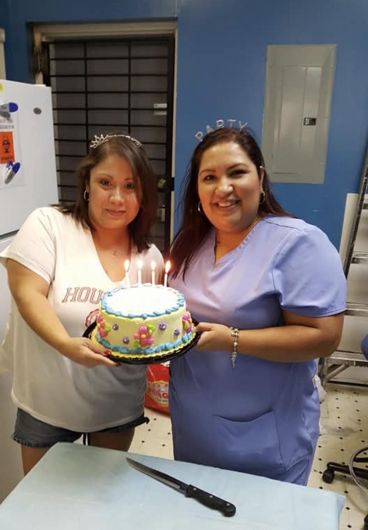 Two women holding a cake with lit candles