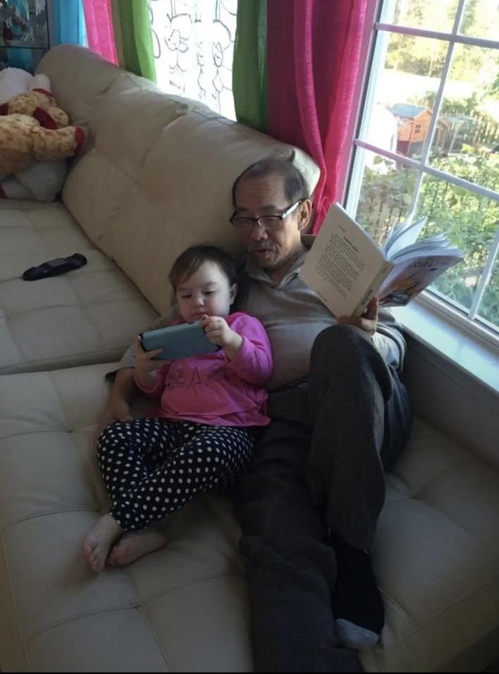 A man and child sitting on a couch reading a book
