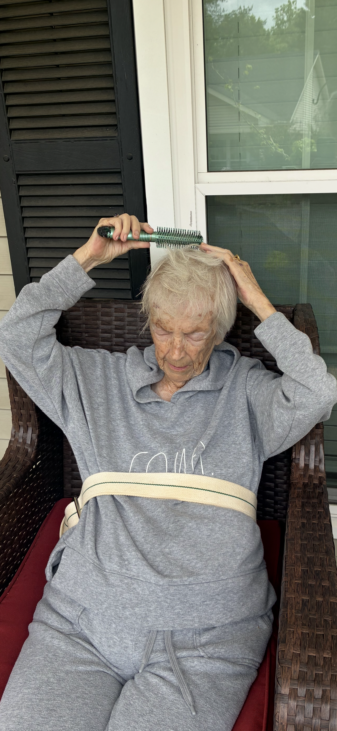 An older woman holding a brush to her head