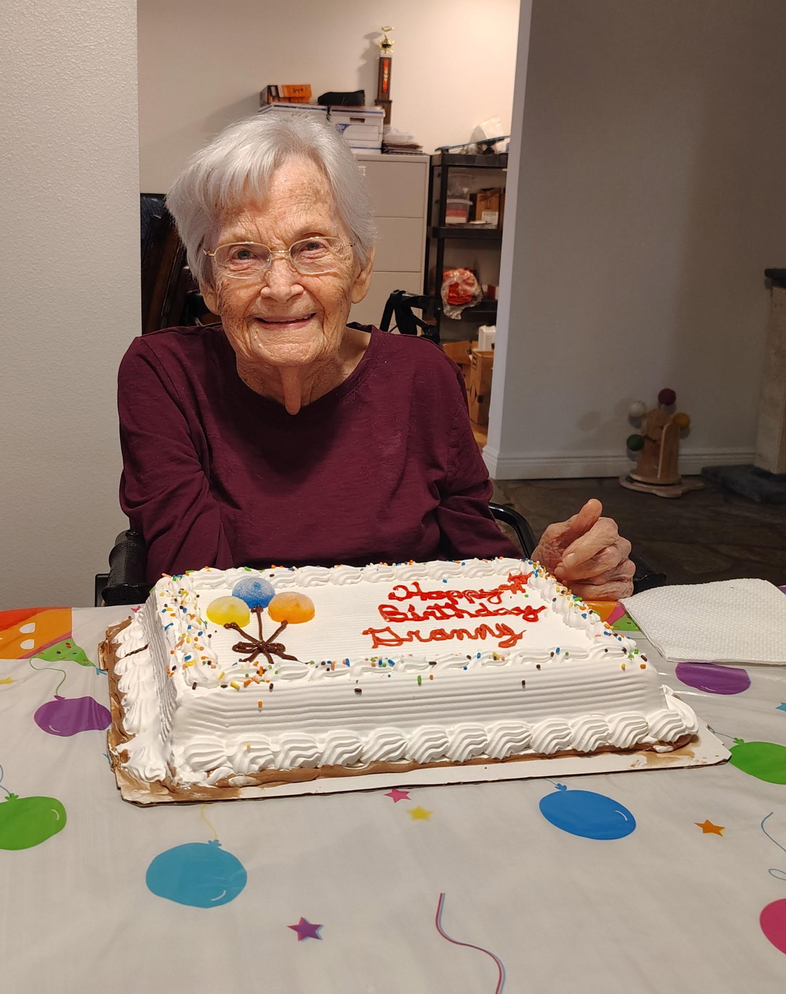 An old woman sitting at a table with a birthday cake
