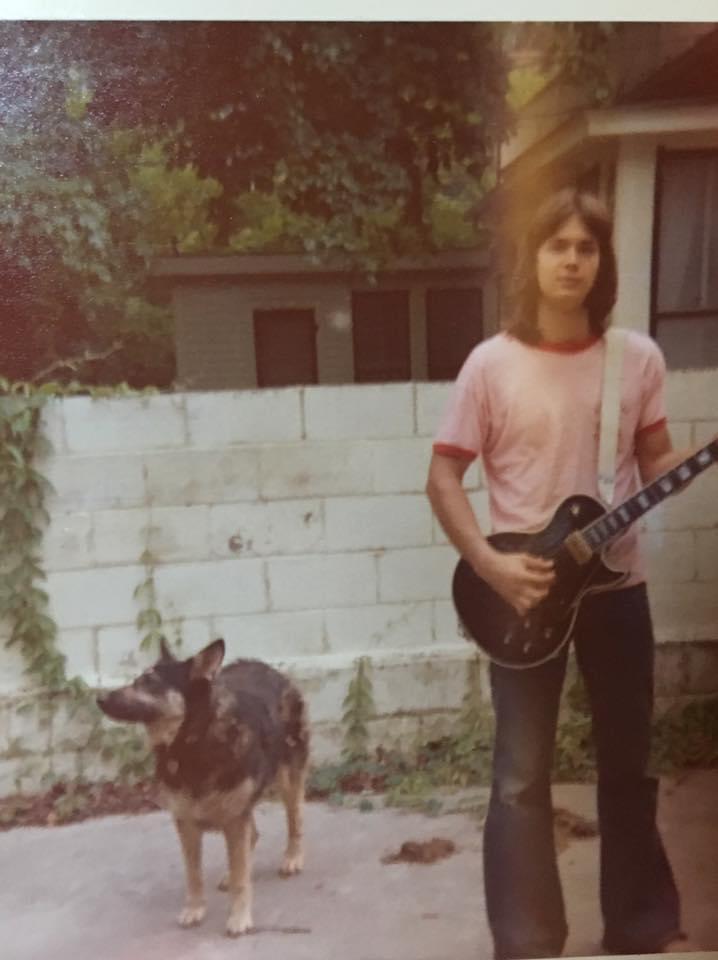 A man holding a guitar and a dog