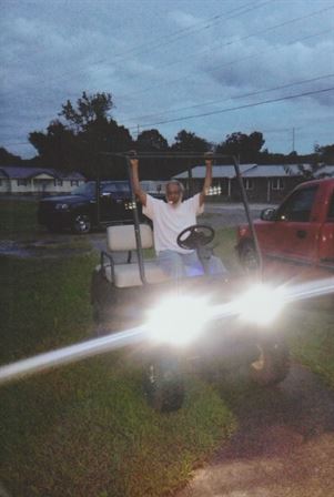 A man in a golf cart with headlights on