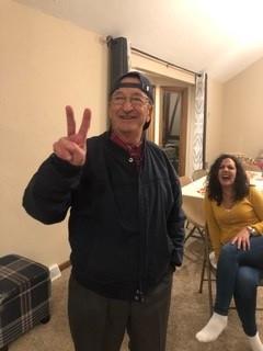 A man in a black jacket and hat holding up two fingers