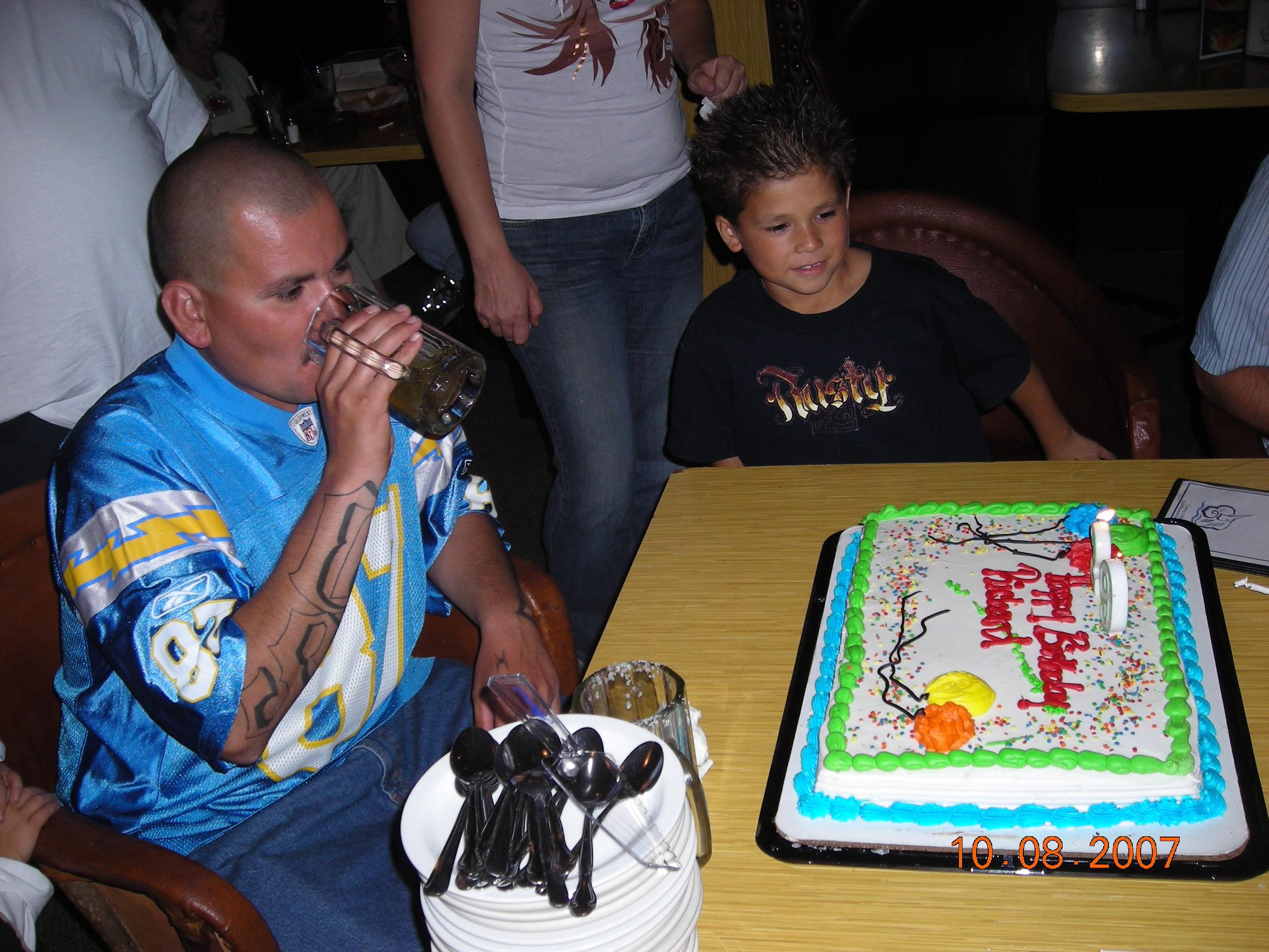 A man drinking from a bottle in front of a birthday cake