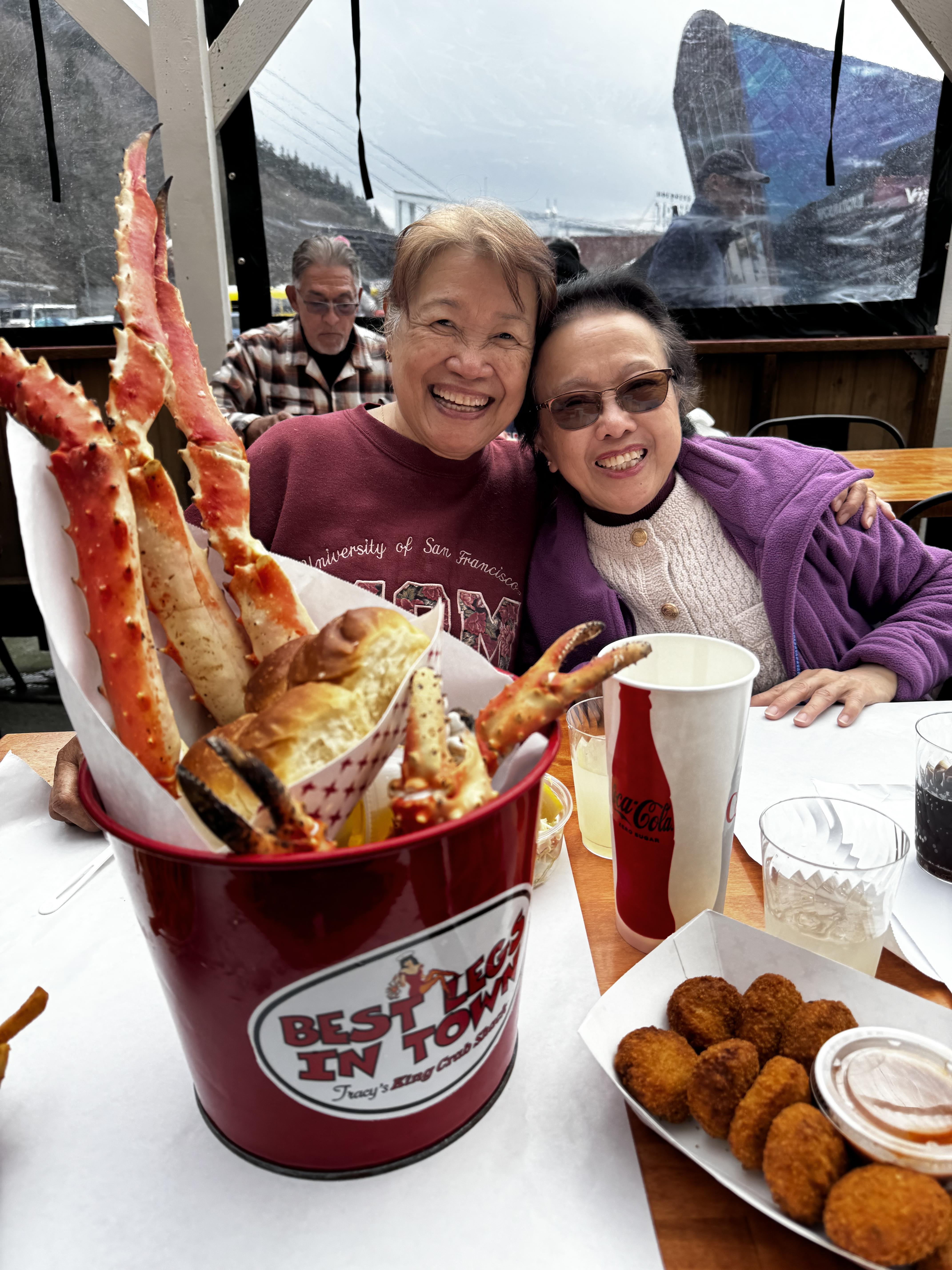 Two women sitting at a table with a bucket of crab sticks
