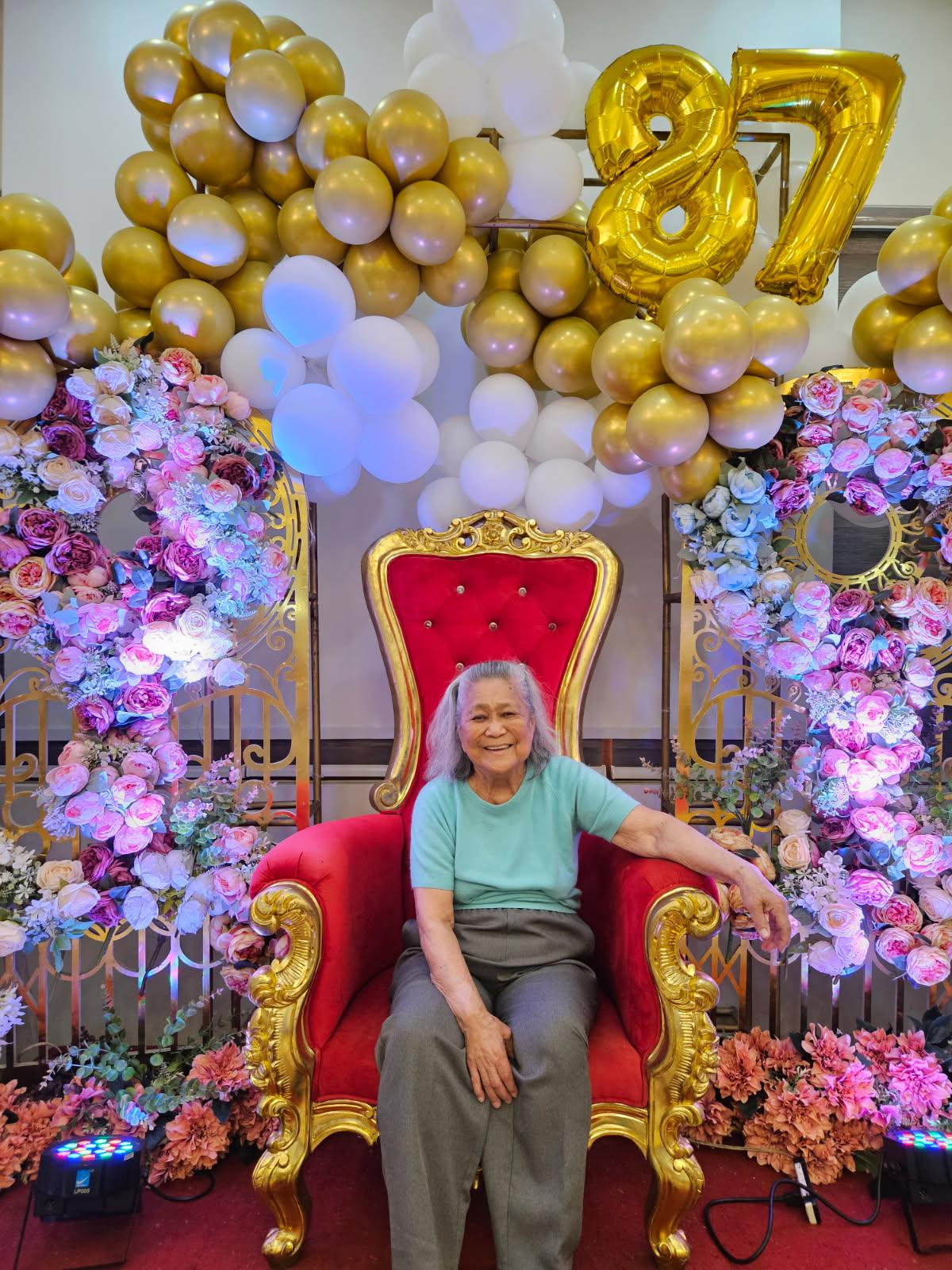 A woman sitting in a red chair with flowers and balloons