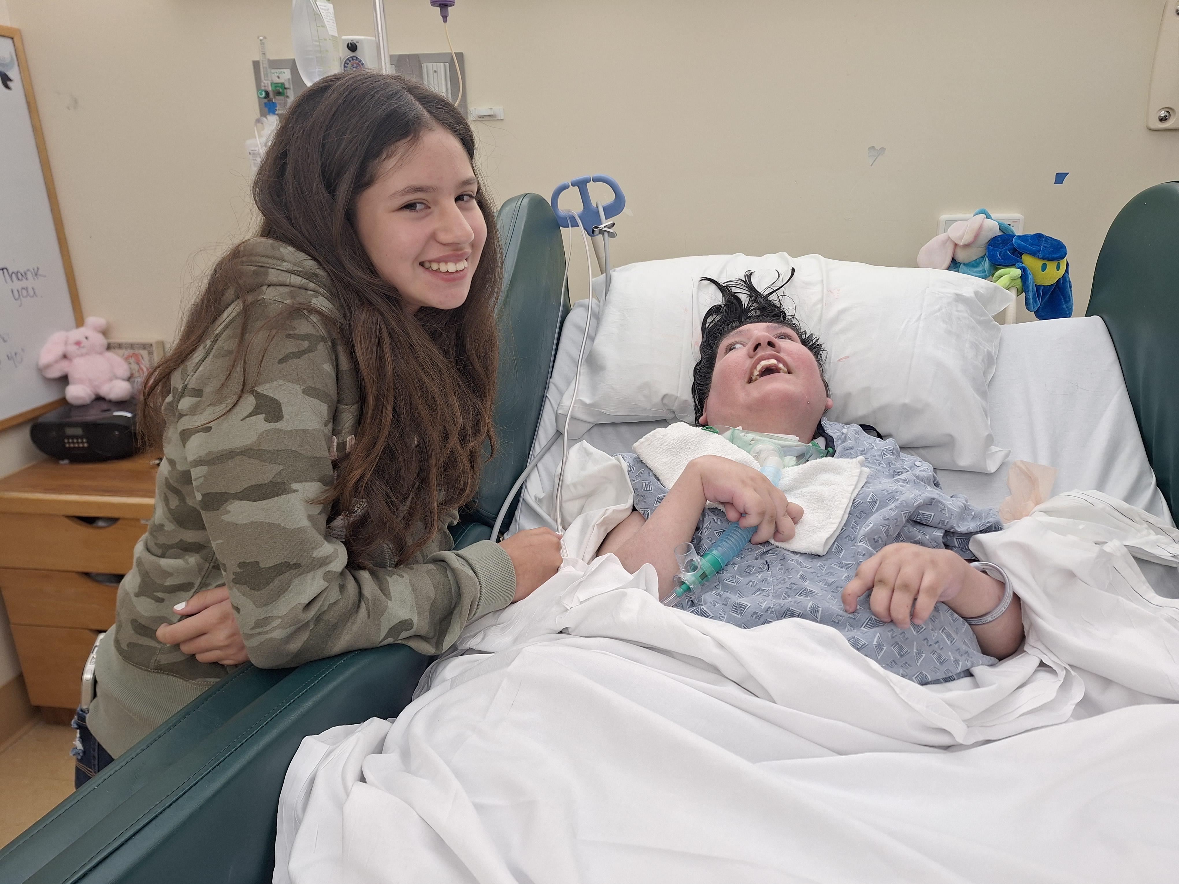 A girl smiling next to a boy in a hospital bed