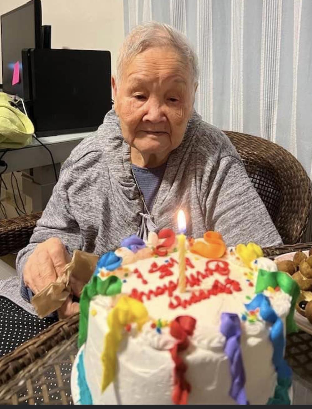 An old woman sitting in front of a cake